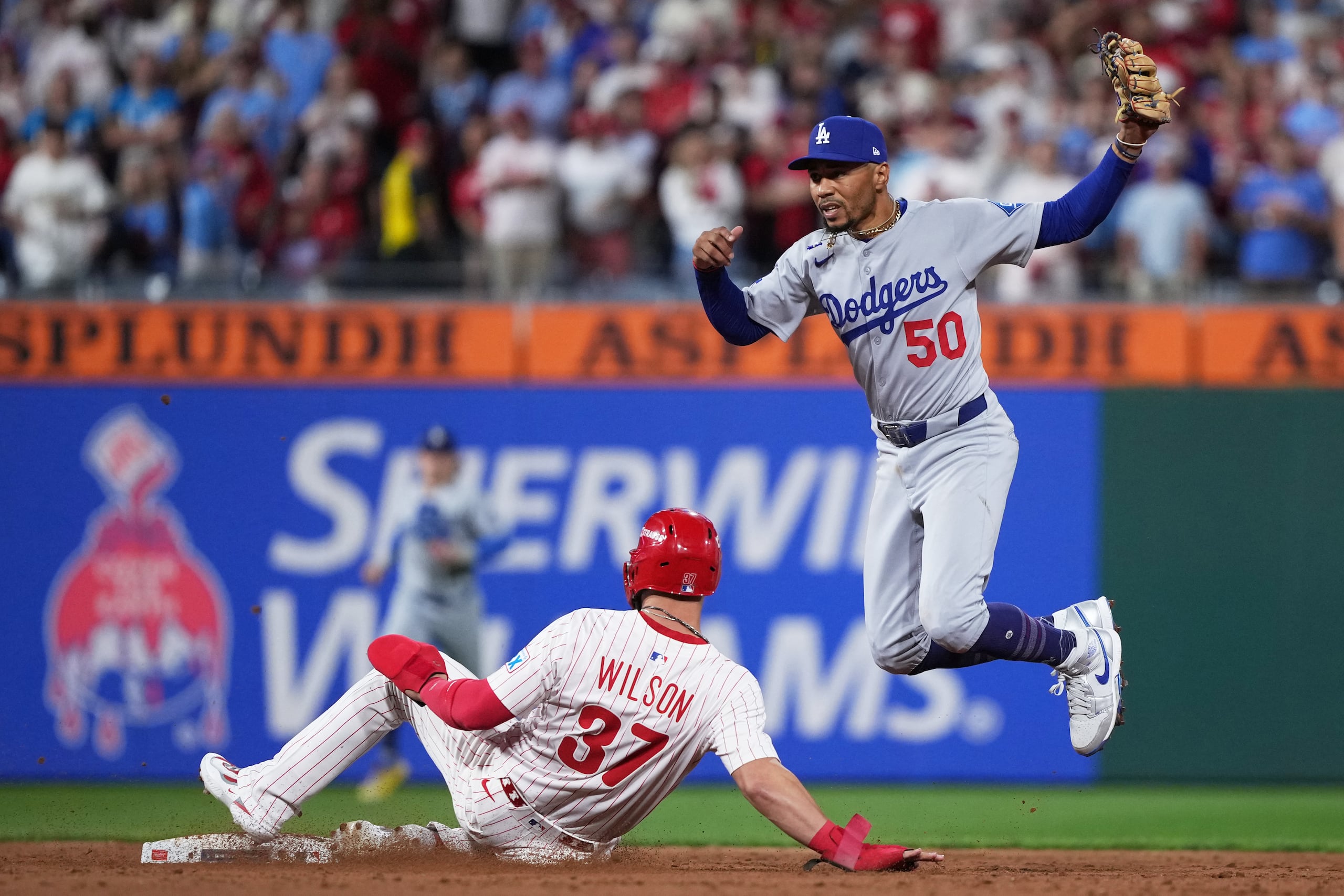 Mookie Betts, derecha, de los Dodgers de Los Ángeles, brinca después de forzar un out a Weston Wilson, de los Filis de Filadelfia, en una jugada de selección durante la novena entrada del segundo juego de la Serie Divisional de la Liga Nacional.