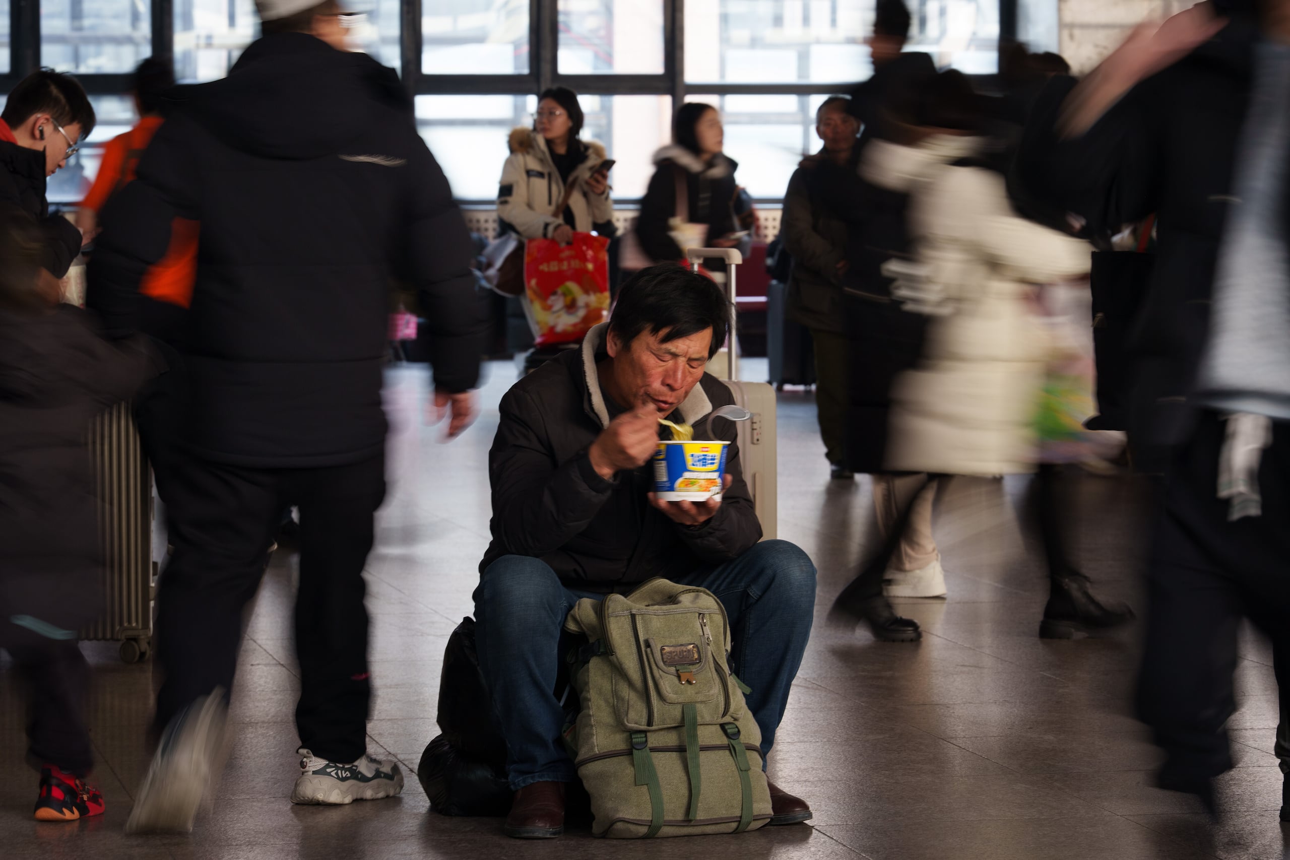 Un viajero come mientras espera en una estación de tren, en la época en la que la gente regresa a su hogar durante el feriado del Año Nuevo Lunar en Beijing, China, el martes 10 de febrero de 2026. (AP Foto/Vincent Thian)