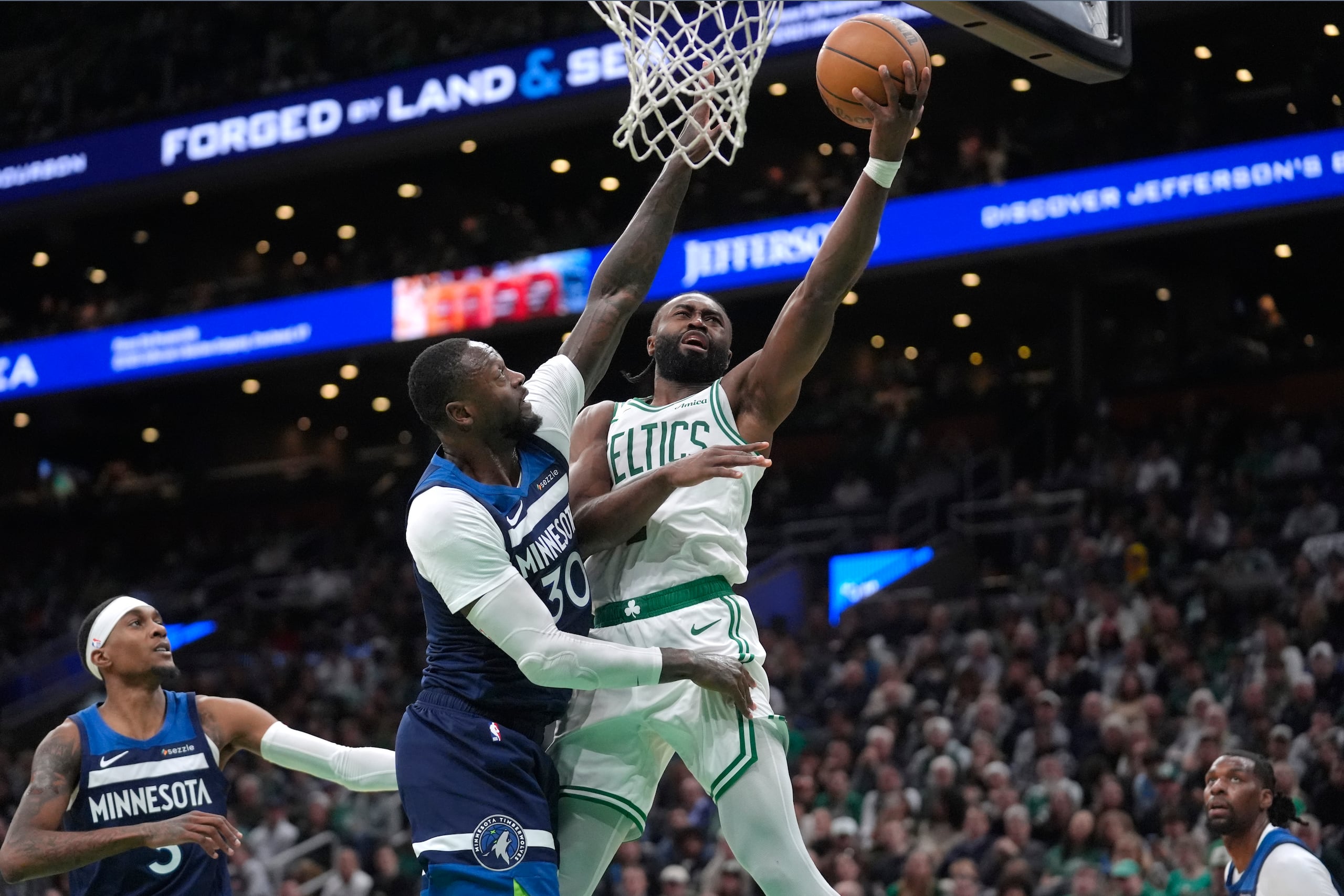 Jaylen Brown, con el balón, de los Celtics de Boston, ataca el aro con Julius Randle (30), de los Timberwolves de Minnesota, intentendo bloquear su tiro.