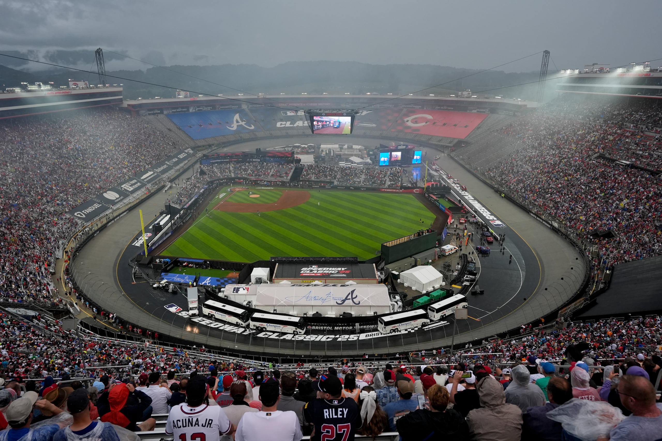 Los fanáticos esperan en la lluvia por ver el partido entre los Reds y Braves en el Bristol Motor Speedway en Tennessee.