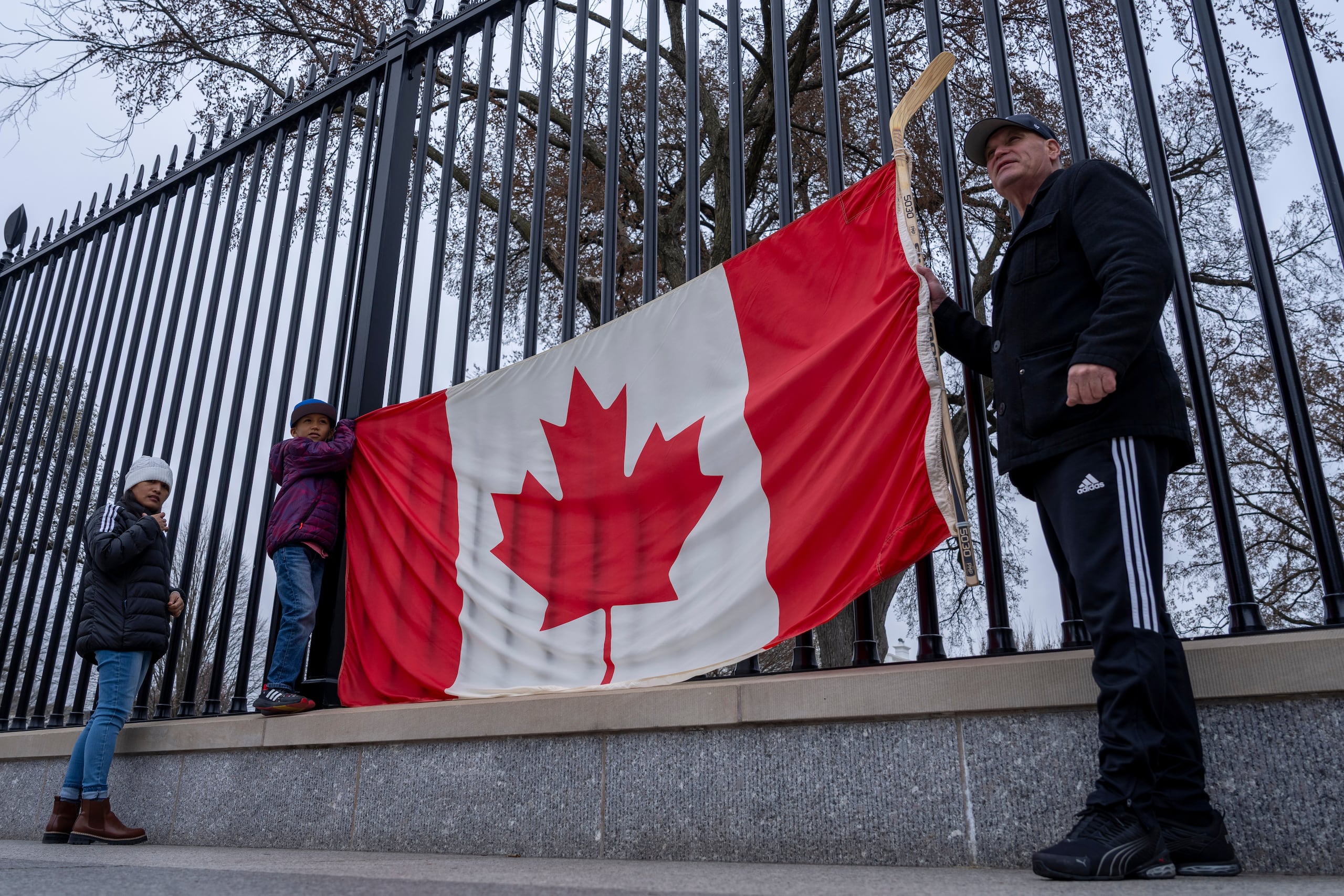 ARCHIVO - De derecha a izquierda, los residentes de Toronto Douglas Bloomfield, su hijo Phoenix y su esposa Ame, quienes se encuentran de vacaciones en Washington, sostienen una bandera canadiense y un palo de hockey sobre hielo para mostrar su apoyo a Canadá en relación con los aranceles comerciales, frente a la Casa Blanca en Washington, el 13 de marzo de 2025. (AP Foto/Ben Curtis/Archivo)