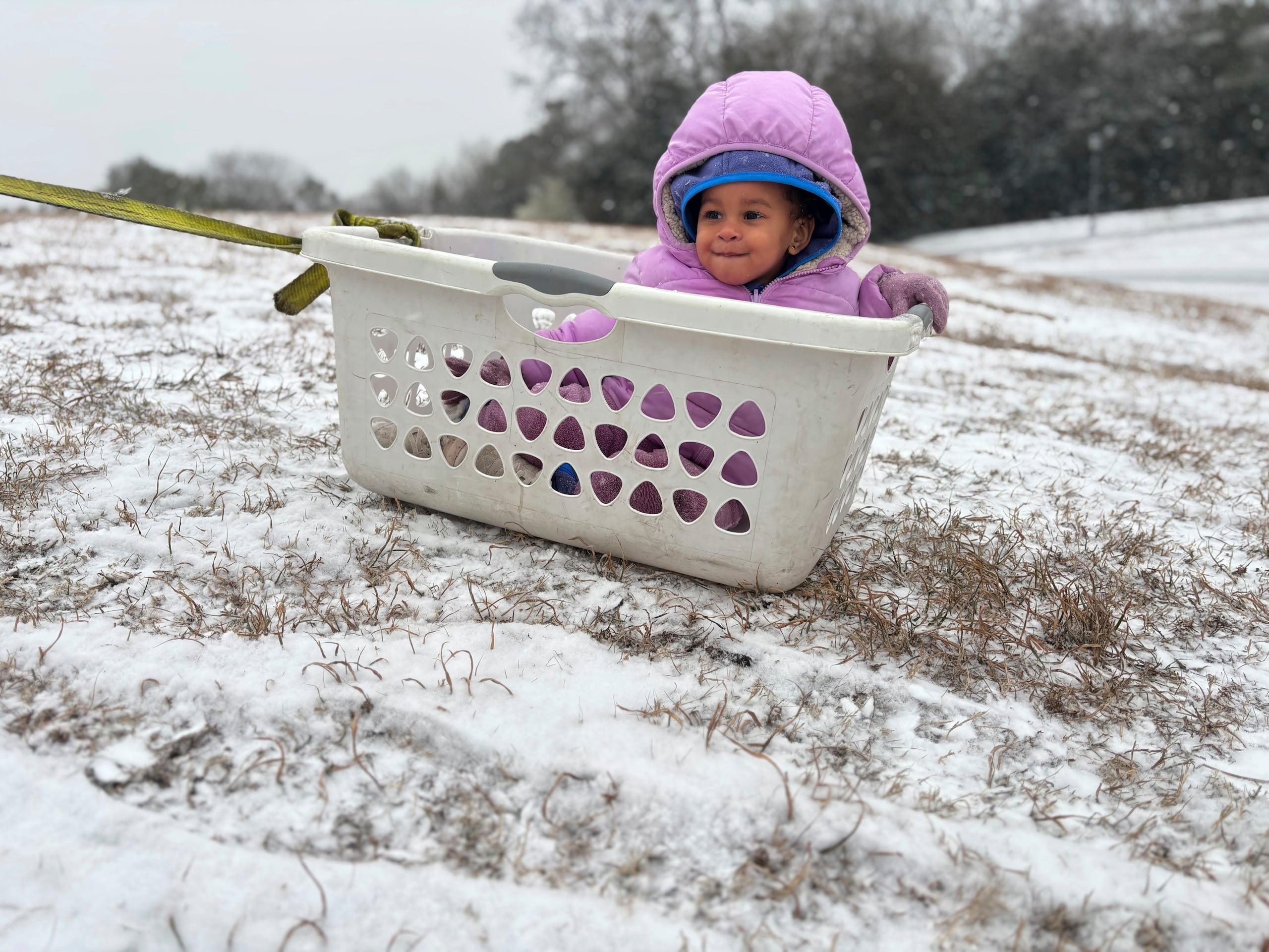 Aria Johnson, de 1 año, juega en la nieve con una cesta como trineo en Montgomery, Alabama, el martes 21 de enero de 2025. (AP Foto/Kim Chandler)