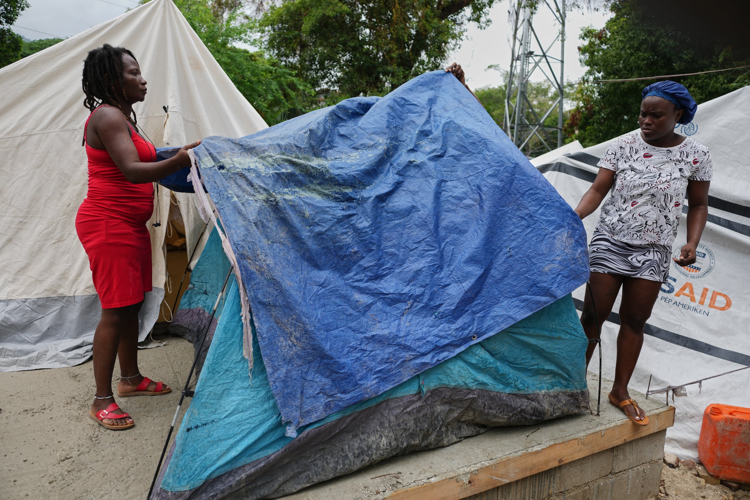 Mujeres colocan toldos sobre sus tiendas de campaña ante la pronosticada lluvia en un refugio para familias desplazadas por la violencia de pandillas en Puerto Príncipe, Haití, el jueves 23 de octubre de 2025. (Foto AP/Odelyn Joseph)