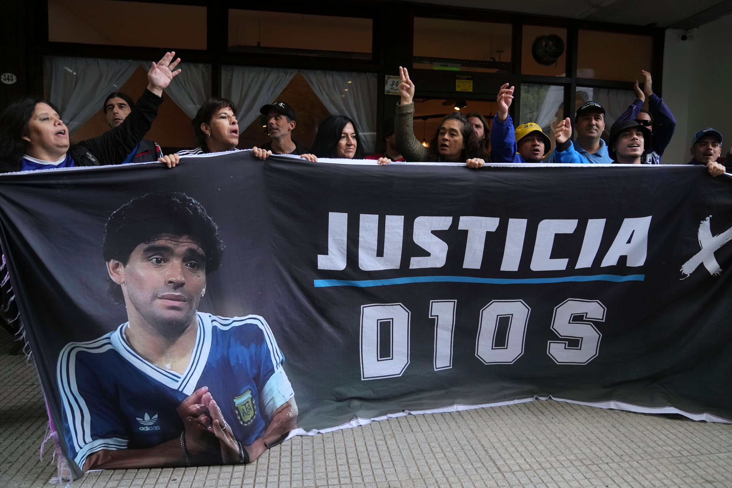 Seguidores del fallecido Diego Maradona sostienen una pancarta con la frase "Justicia para Dios" afuera del tribunal donde se realiza el juicio de homicidio por negligencia contra el personal médico que trató a Maradona, el martes 11 de marzo de 2025, en las afueras de Buenos Aires.