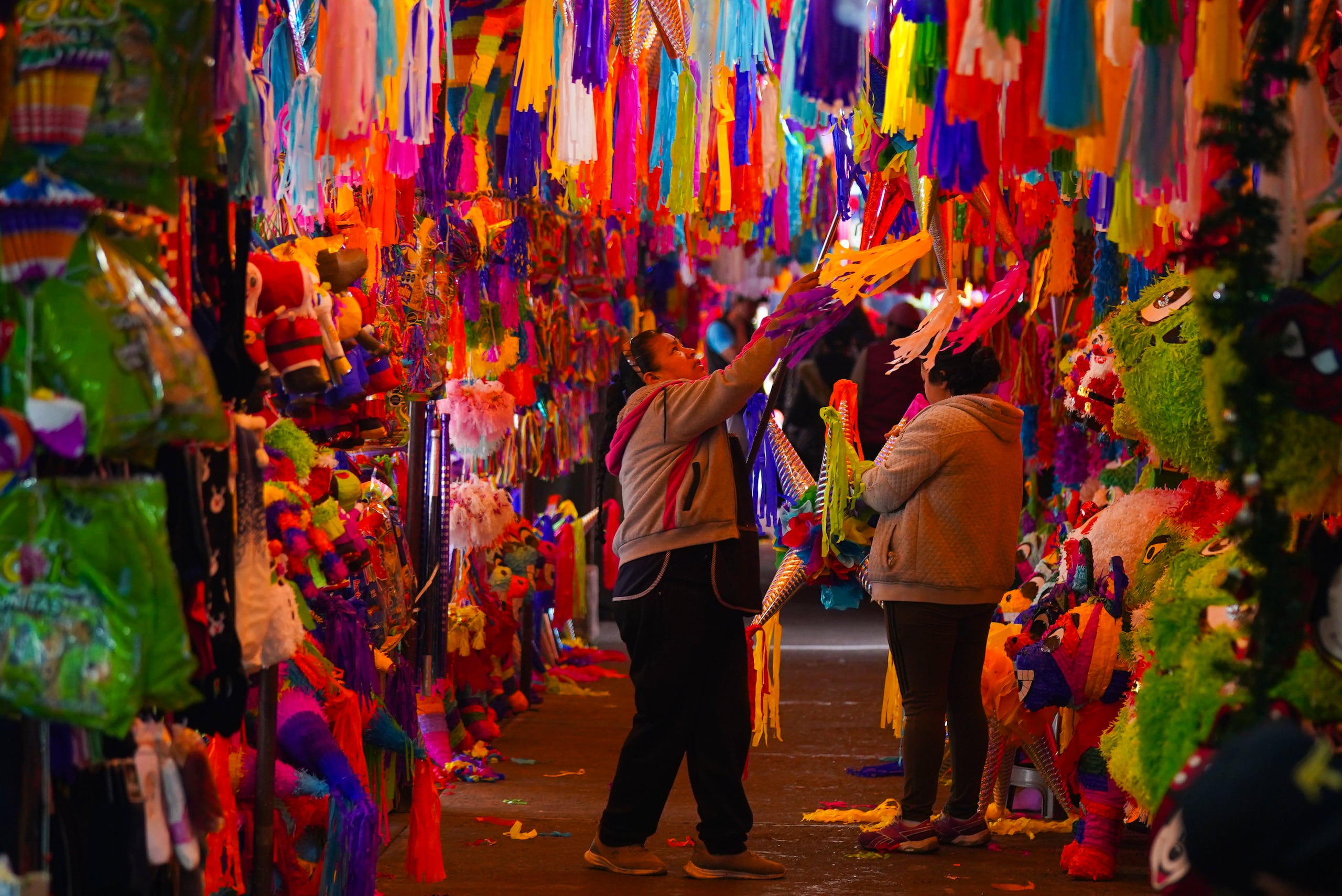 A vendor lowers a piñata for a customer at the Jamaica market in Mexico City, Thursday, Dec. 14, 2023. The breaking open of piñatas are part of the Mexican Christmas tradition. (AP Photo/Fernando Llano)
