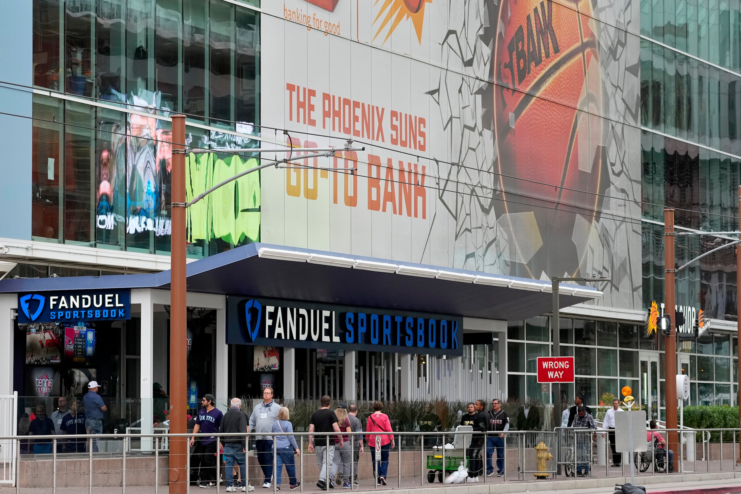 Fanáticos caminan a un lado de una casa de apuestas integrada al Footprint Center, el martes 14 de marzo de 2023, en Phoenix. El Béisbol Grandes Ligas, por muchos años la liga más renuente a la apertura de las apuestas, ahora permite que sus jugadores sean embajadores de las compañías de apuestas.