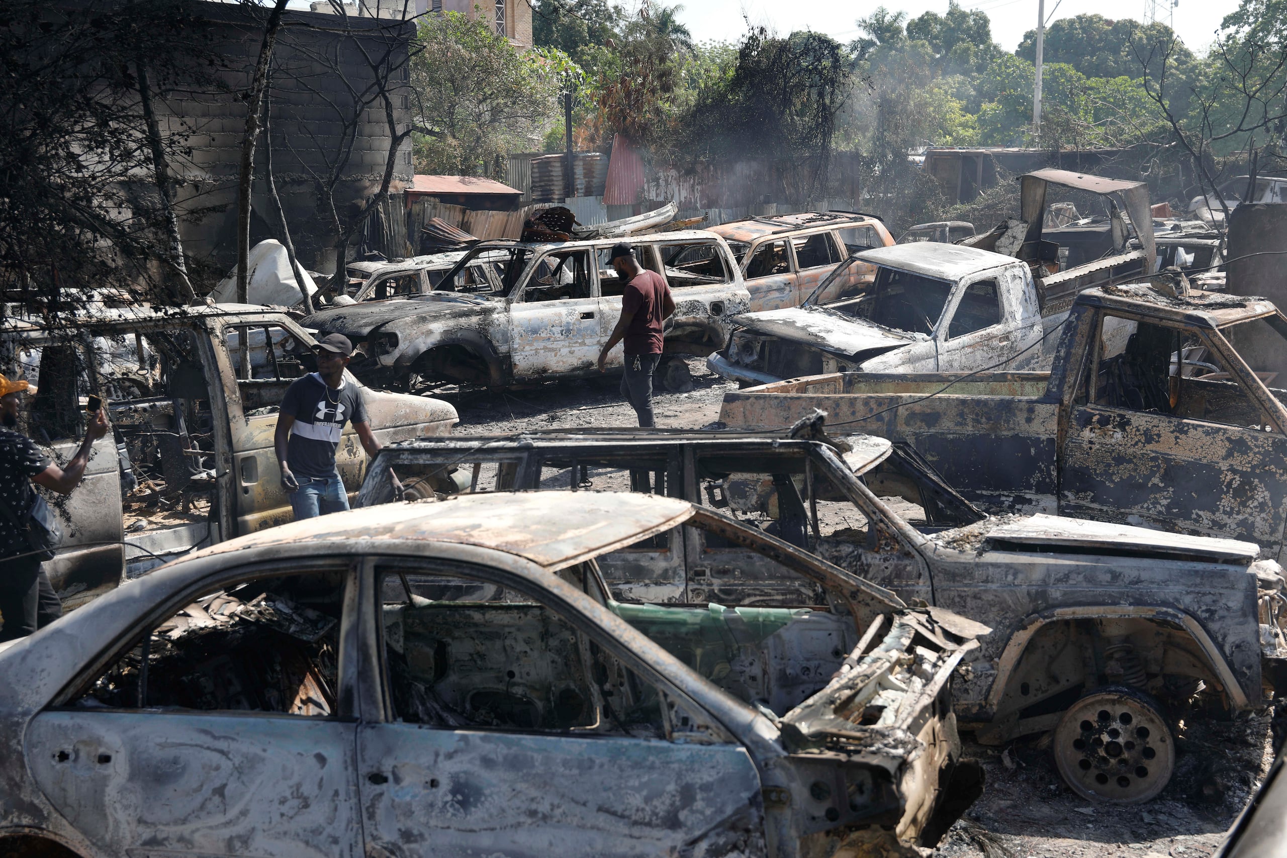 Varias personas buscan piezas rescatables de coches quemados en un taller mecánico incendiado durante la violencia desatada por pandillas armadas en Puerto Príncipe, Haití, el lunes 25 de marzo de 2024. (AP Foto/Odelyn Joseph)