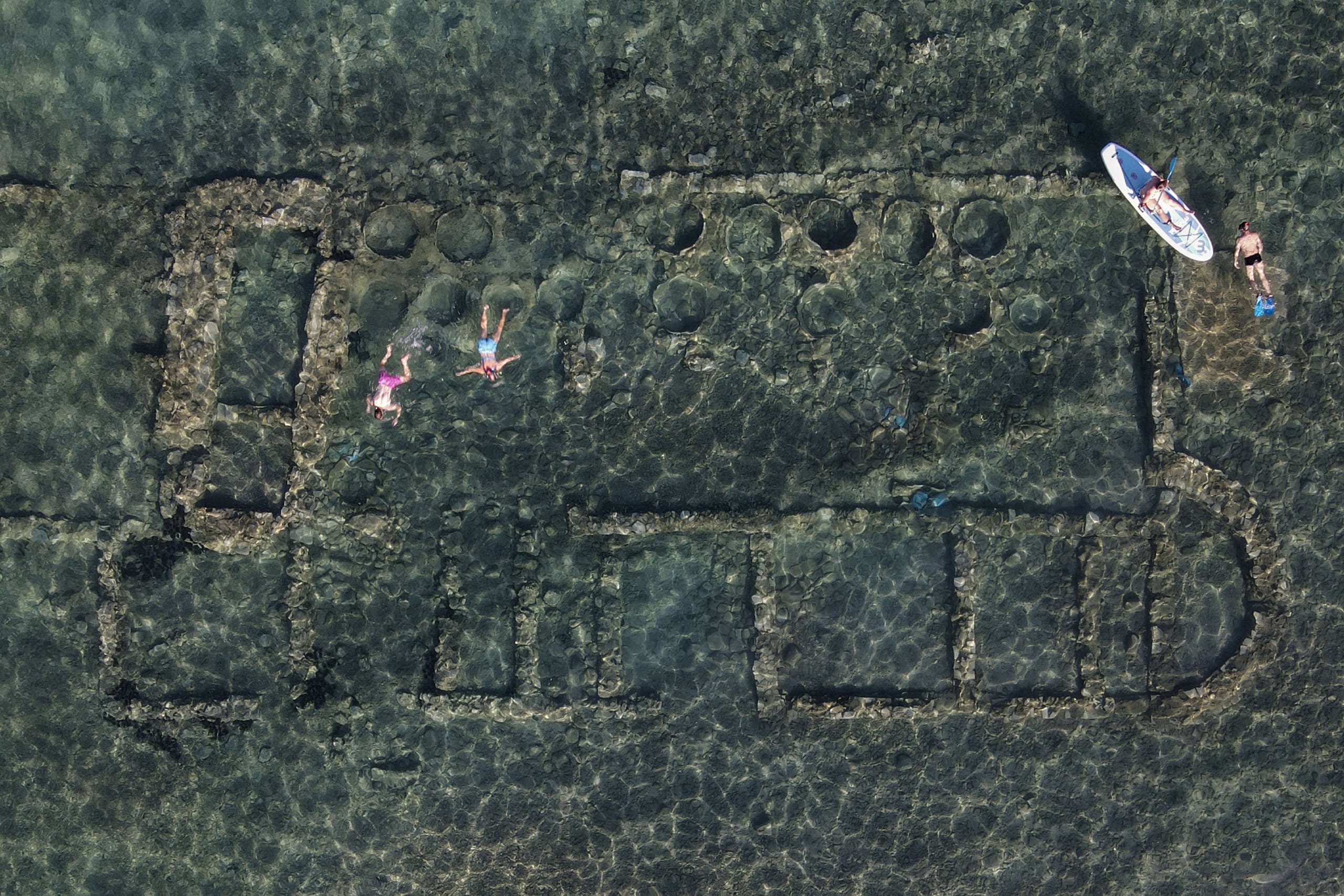 People swim to explore the ancient 'Sunken City' in Ancient Epidavros, in Peloponeese peninsula , southern Greece on August 7, 2023. Sunken City is a small settlement which might have been a trading post in ancient times, and lays underwaters some 50 meters from the coast of today's Epidavros. (Photo by Louisa GOULIAMAKI / AFP)