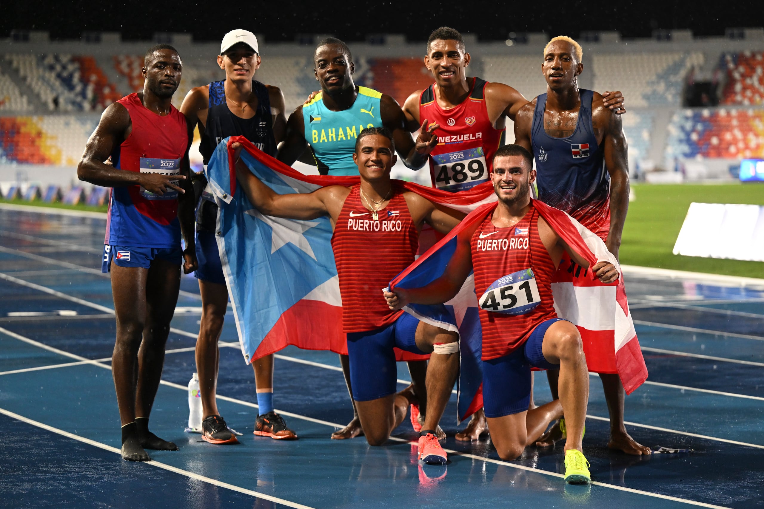 Ayden Owens y Yariel Soto posan, banderas en manos, al concluir el evento de los 1,500 metros junto a otros competidores.