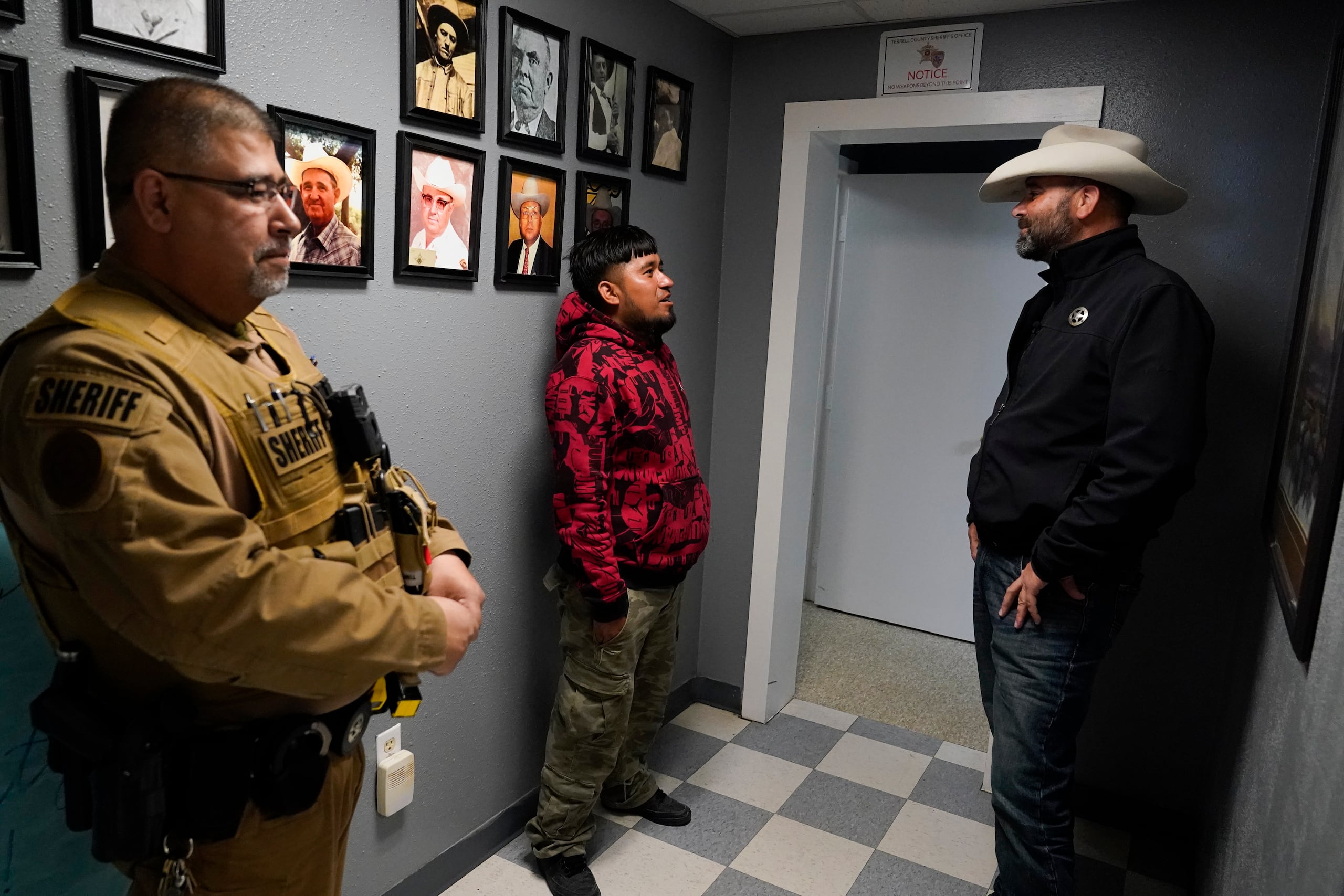 El jefe de policía del condado Terrell, Thaddeus Cleveland, habla con un migrante mexicano recientemente detenido, mientras el sargento Manuel Jimenez permanece a un costado, en el Departamento de Policía del condado Terrell, el jueves 21 de marzo de 2024, en Sanderson, Texas. (AP Foto/Erik Verduzco)