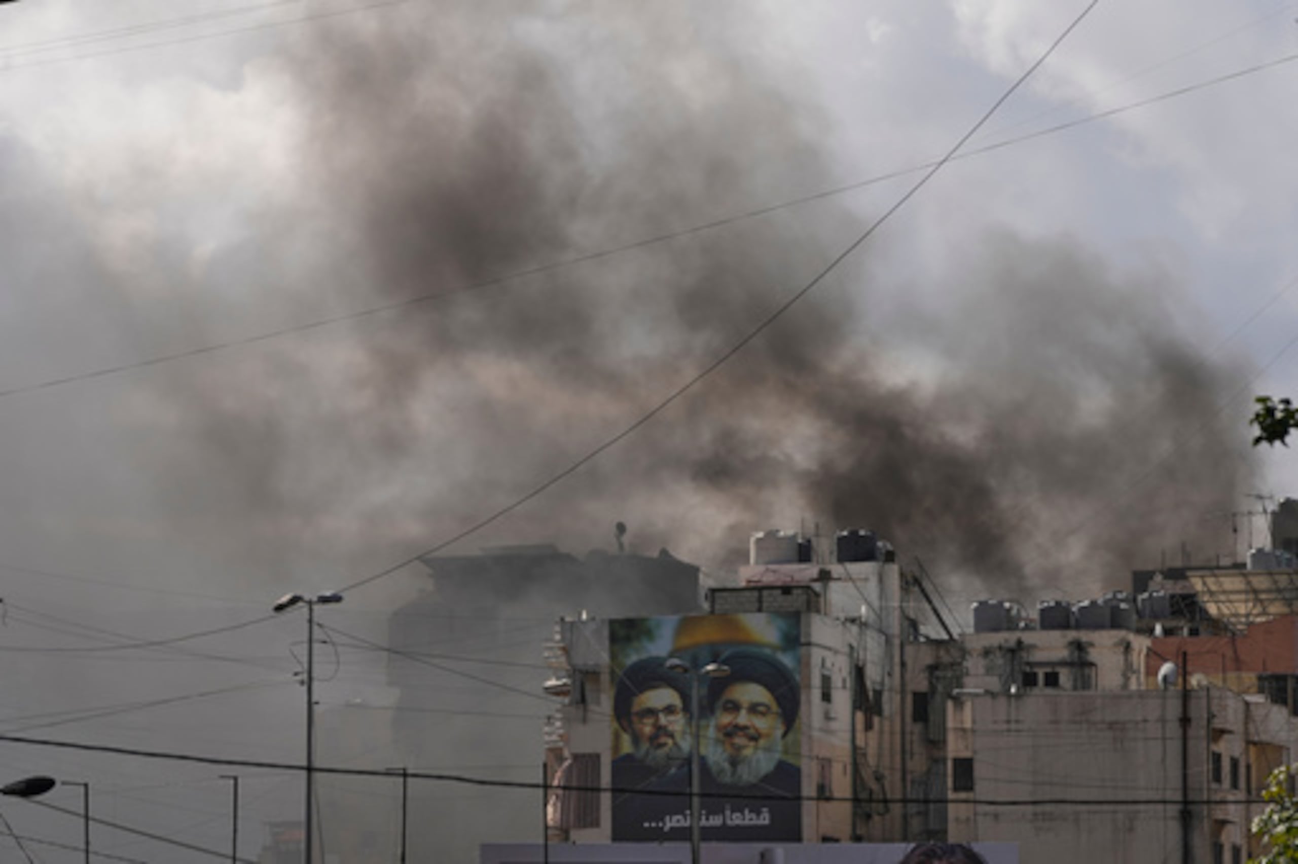 Retratos de los fallecidos líderes de Hezbollah Hassan Nasrallah, a la derecha, y su primo, Hashem Safieddine, se ven cerca de la humareda provocada por un ataque aéreo israelí en Dahiyeh, un suburbio al sur de Beirut, en Líbano. (AP Foto/Hassan Ammar)