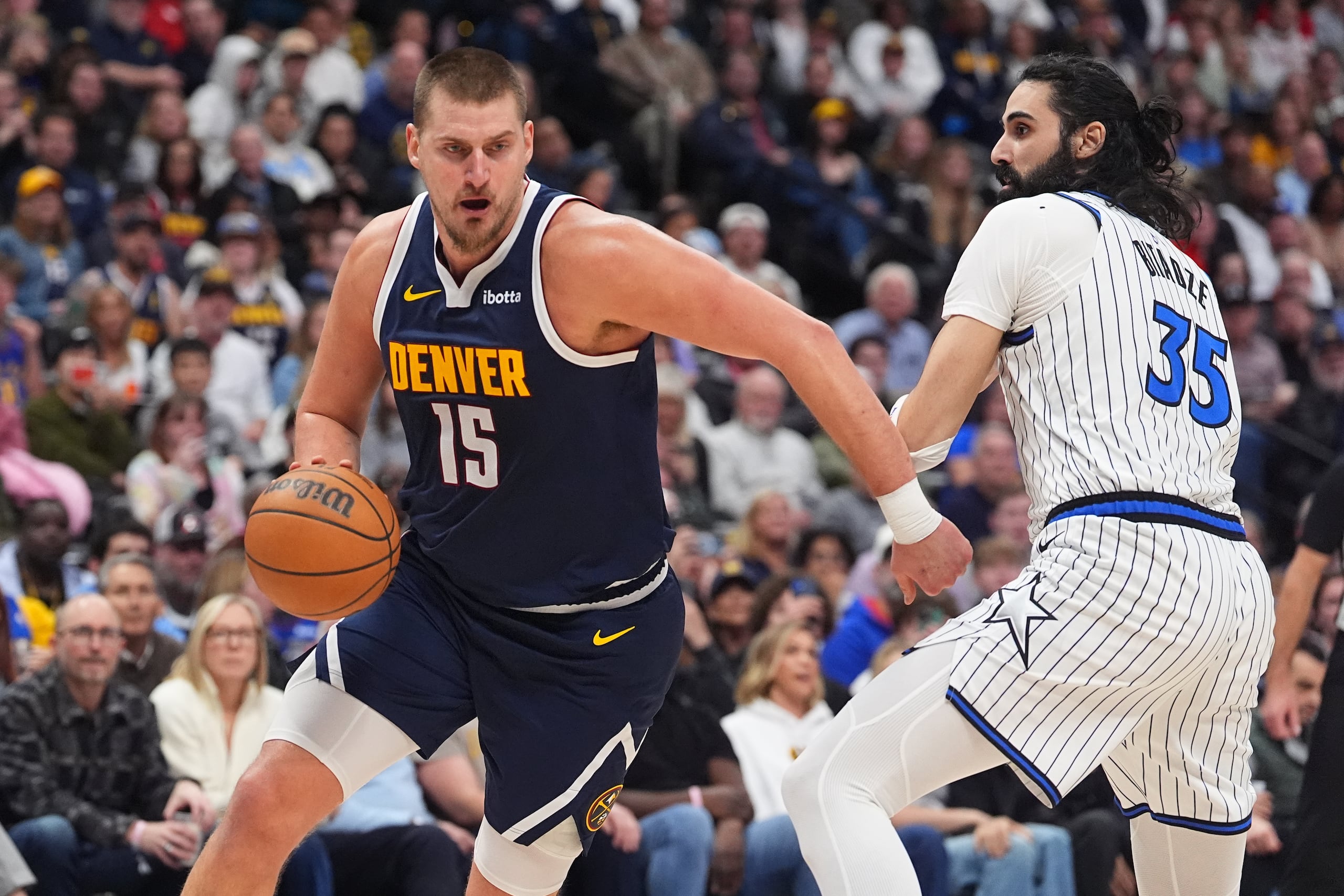 El centro de los Nuggets de Denver, Nikola Jokić (15), avanza hacia la canasta frente al centro de los Magic de Orlando, Goga Bitadze (35), en la segunda mitad de un juego de baloncesto de la NBA el jueves 18 de diciembre de 2025, en Denver. (AP Photo/David Zalubowski)