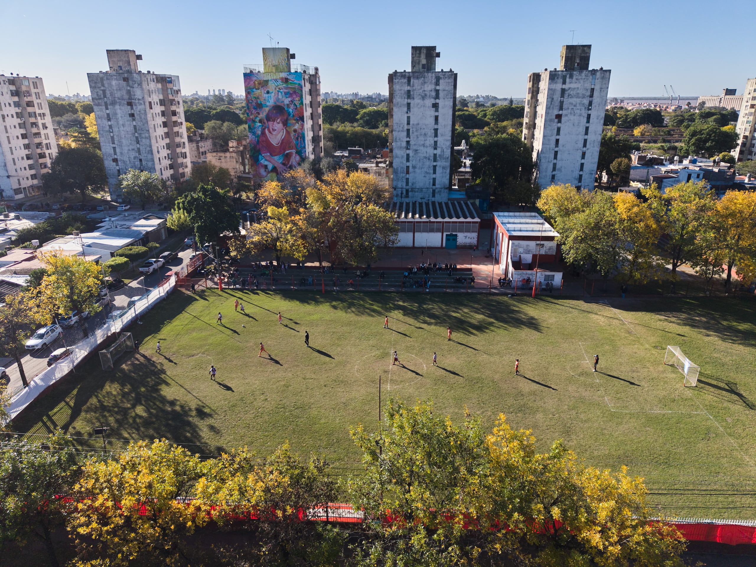 Un mural de Lionel Messi cubre el muro de un edificio mientras un grupo de niños disputan un partido de fútbol en el club Grandoli, donde Messi jugó de niño en Rosario, Argentina, el sábado 2 de mayo de 2026. (AP Foto/Rodrigo Abd)