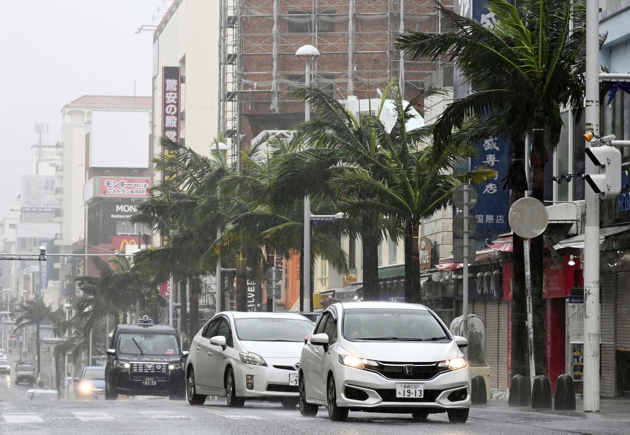 Vehículos manejan por una calle con con fuerte viento en Naha, prefectura de Okinawa, en el sur de Japón, el domingo 6 de agosto de 2023. (Kyodo News via AP)