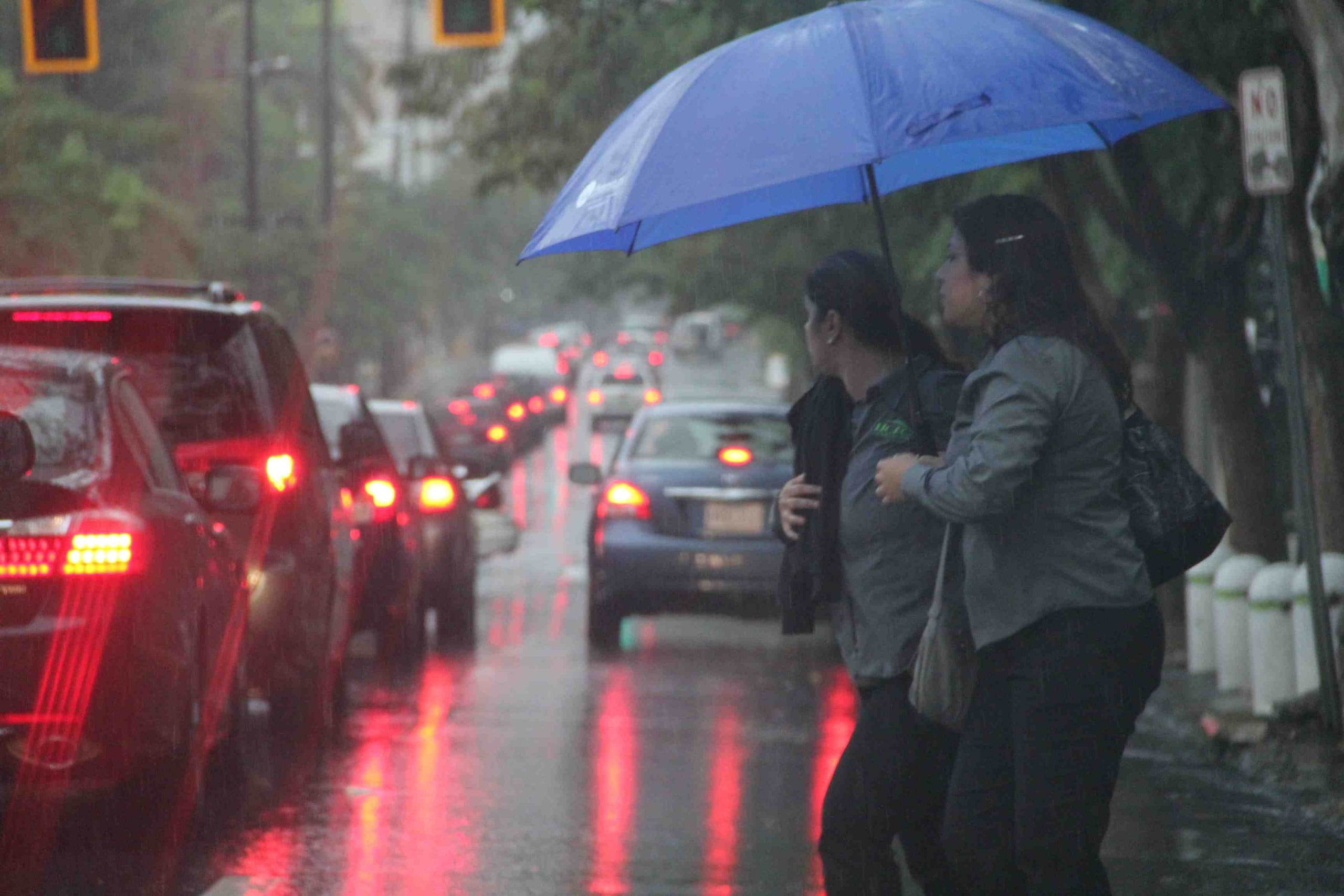 Dos mujeres intentan cruzar una carretera cubiertas por una sombrilla. (GFR Media)