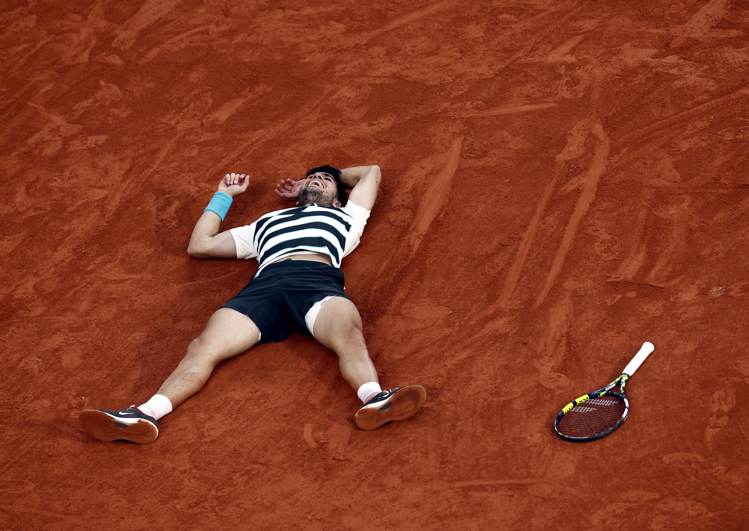 El tenista español, Carlos Alcaraz, celebra lleno de emociones y sobre el barro de la cancha principal del Abierto de Francia su victoria de dos sets abajo en la final de Roland Garros sobre el italiano Jannik Sinner.