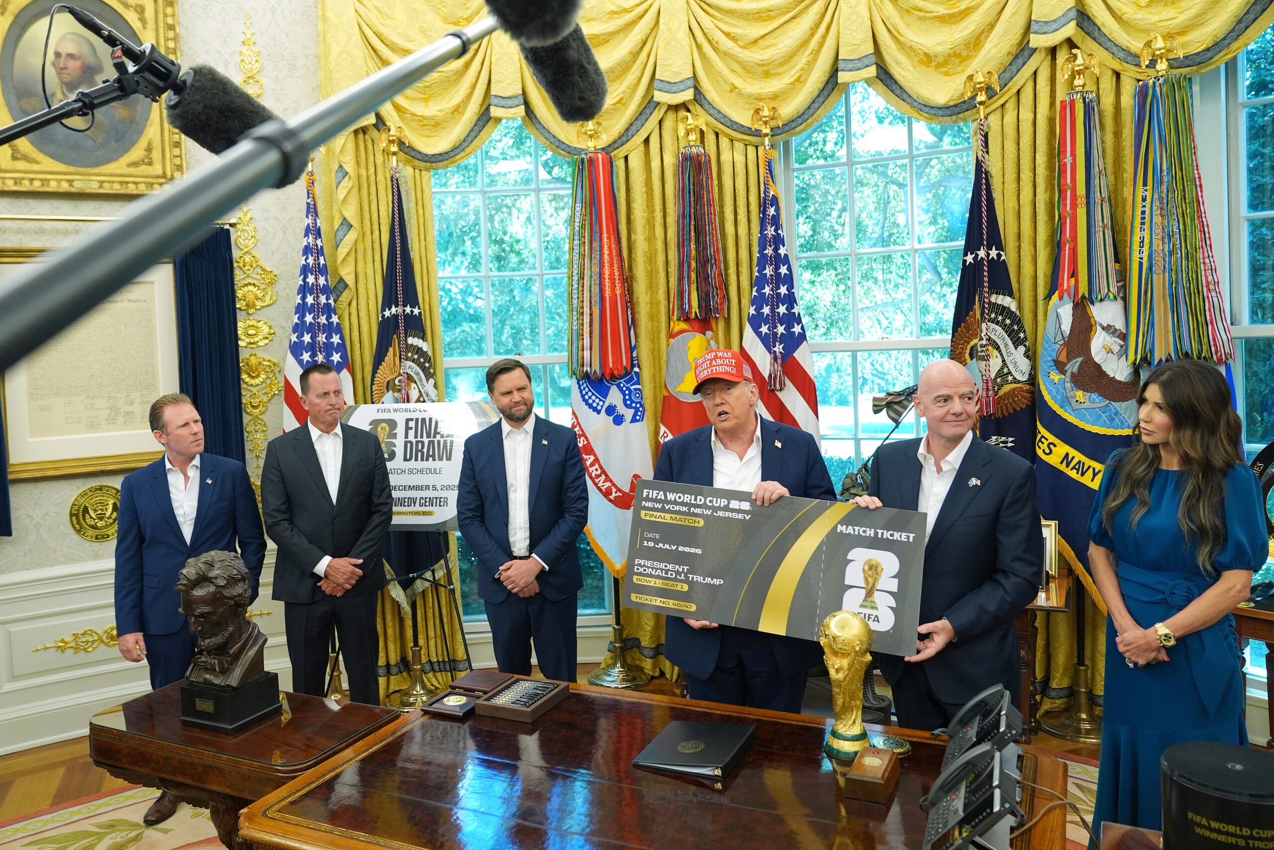 ARCHIVO - Fotodel 22 de agosto del 2025, el presidente Donald Trump habla en la Oficina Oval de la Casa Blanca cargando una representación gigante del boleto al Mundial acompañado por el presidente de la FIFA Gianni Infantino, además de Andrew Giuliani, Richard Grenell, presidente de la junta de gobierno del Kennedy Center, el vicepresidente JD Vance y la secretaria de seguridad interior Kristi Noem. (AP Foto/Jacquelyn Martin, Archivo)