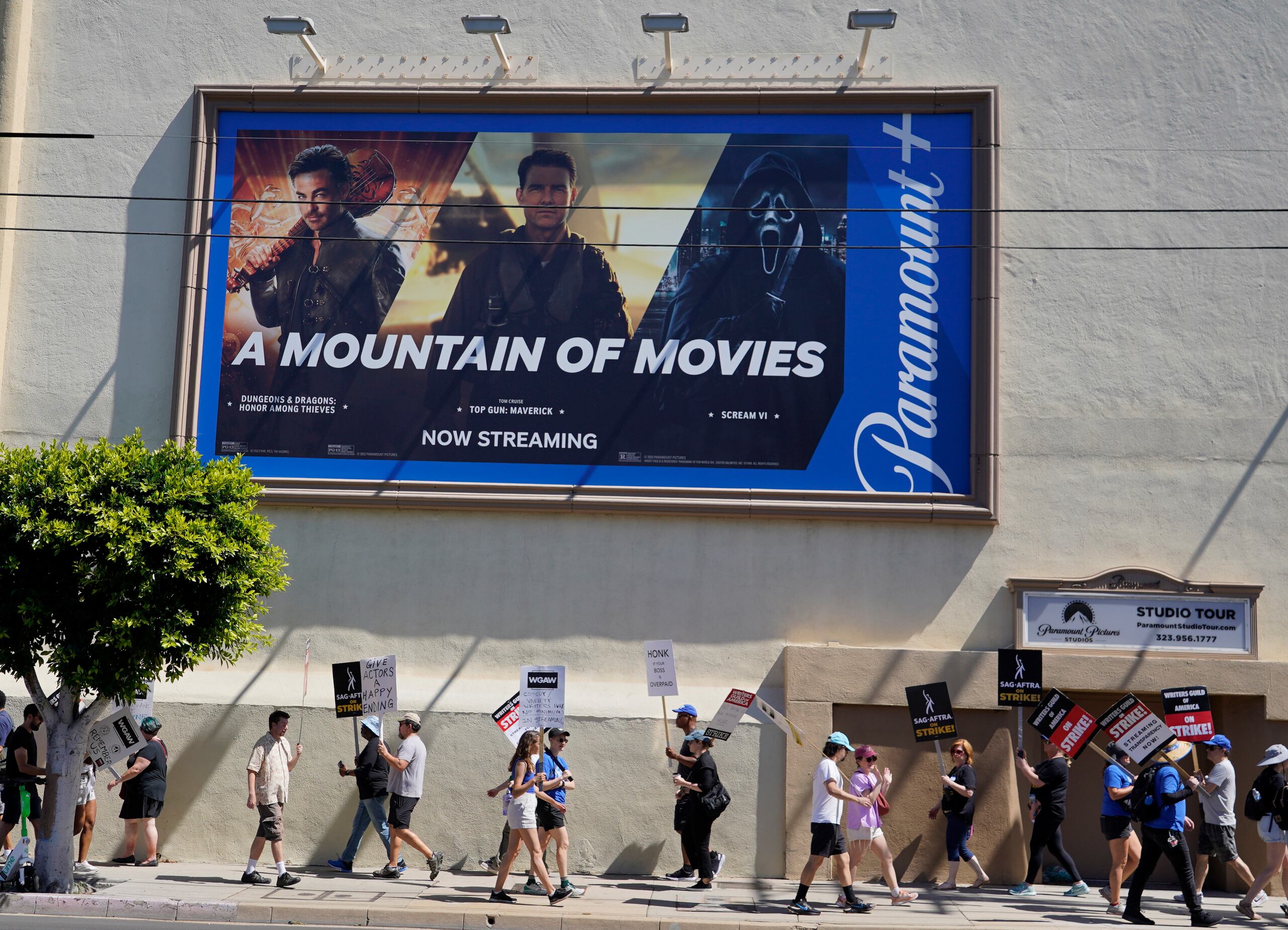 Un anuncio de Paramount+ se puede ver en un edificio de la casa productora, mientras escritores y actores caminan con cartelones manifestando su posición ante la huelga en Hollywood.