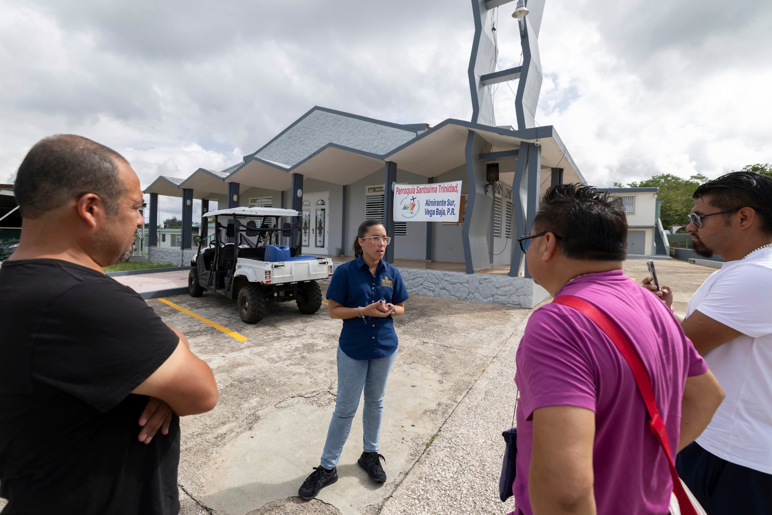 Una guía habla con visitantes en el exterior de la iglesia de la parroquia de la Santísima Trinidad, donde Bad Bunny fue monaguillo, en Vega Baja, Puerto Rico, el 12 de agosto de 2025. (AP Foto/Alejandro Granadillo)