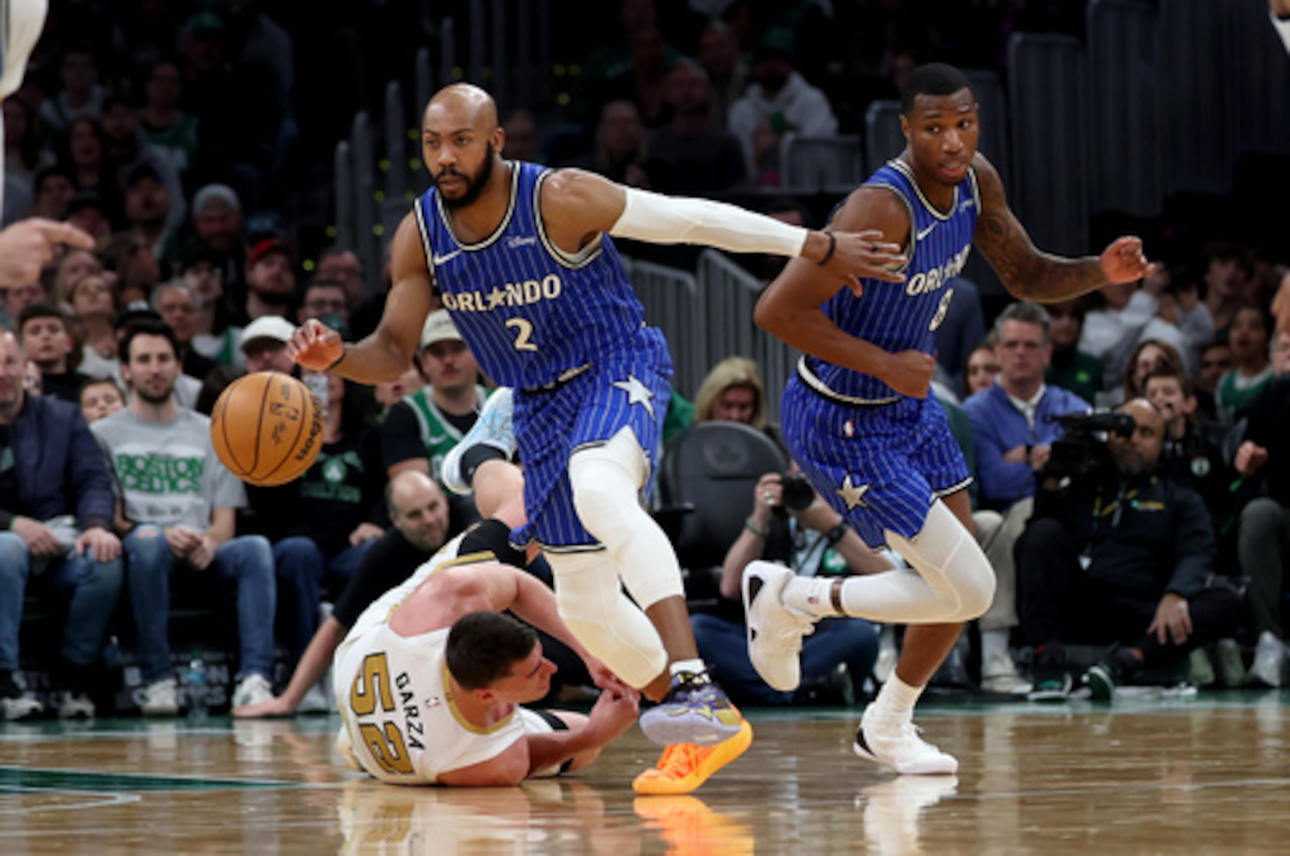 El alero de los Boston Celtics Luka Garza (52) cae a la cancha mientras el escolta de los Orlando Magic Jevon Carter (2) y el alero Jamal Cain (8) toman el control del balón durante la segunda mitad de un partido de baloncesto de la NBA, el domingo 12 de abril de 2026, en Boston. (AP Photo/Mark Stockwell)