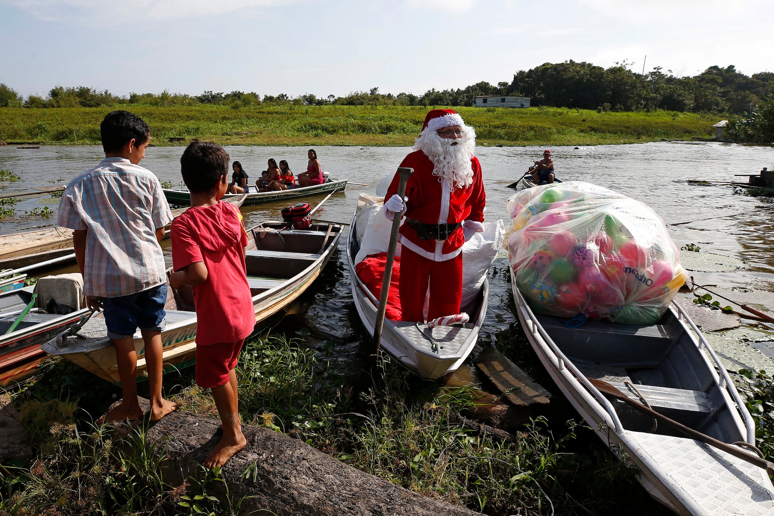 Jorge Barroso, vestido como Santa Claus, llega en un bote a distribuir regalos de Navidad a los niños que viven en las comunidades ribereñas de la Amazonía, en Iranduba, Brasil, el sábado 21 de diciembre de 2024. (AP Foto/Edmar Barros)