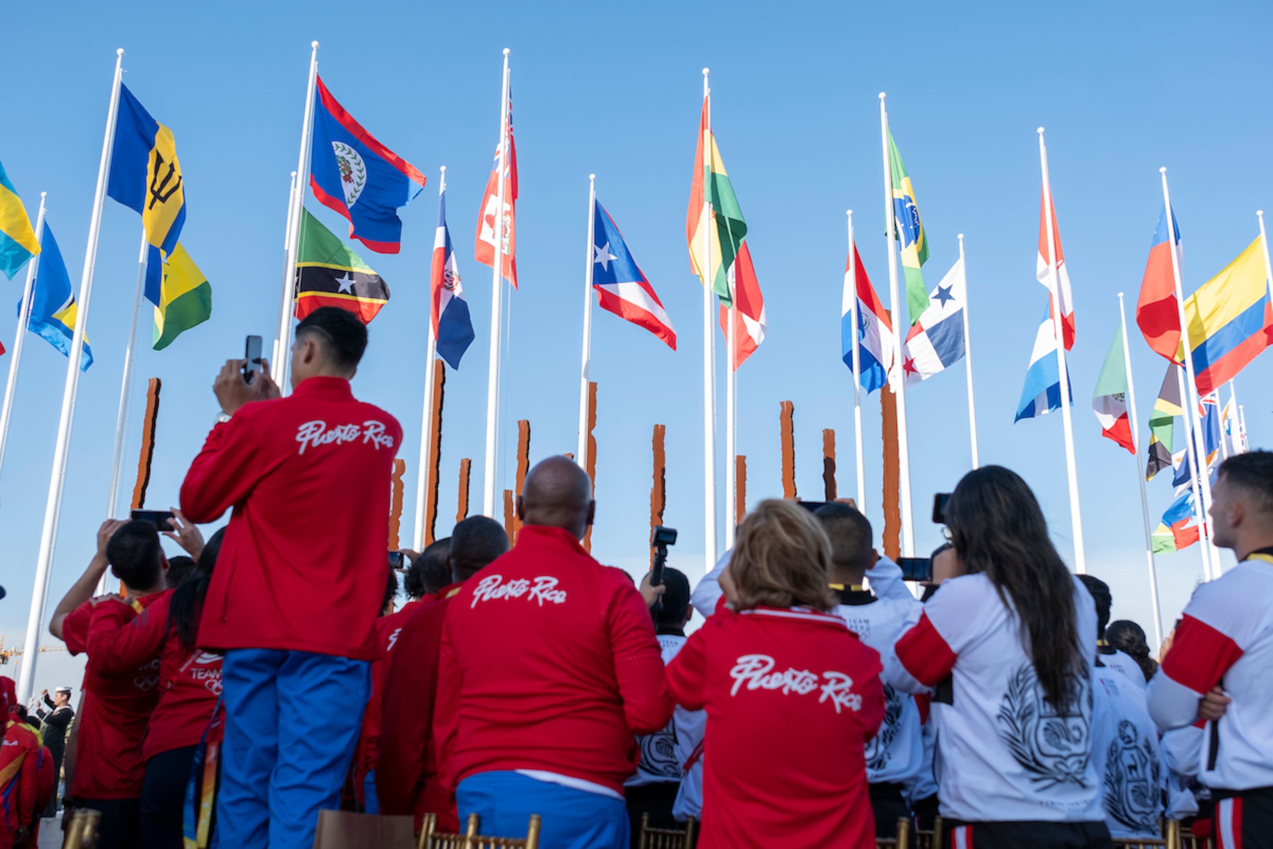 Un grupo de atletas, entrenadores y directivos de Puerto Rico observan la bandera de Puerto Rico al ser izada en la Villa Panamericana en Santiago. (Luis Licona / Straffon Images)