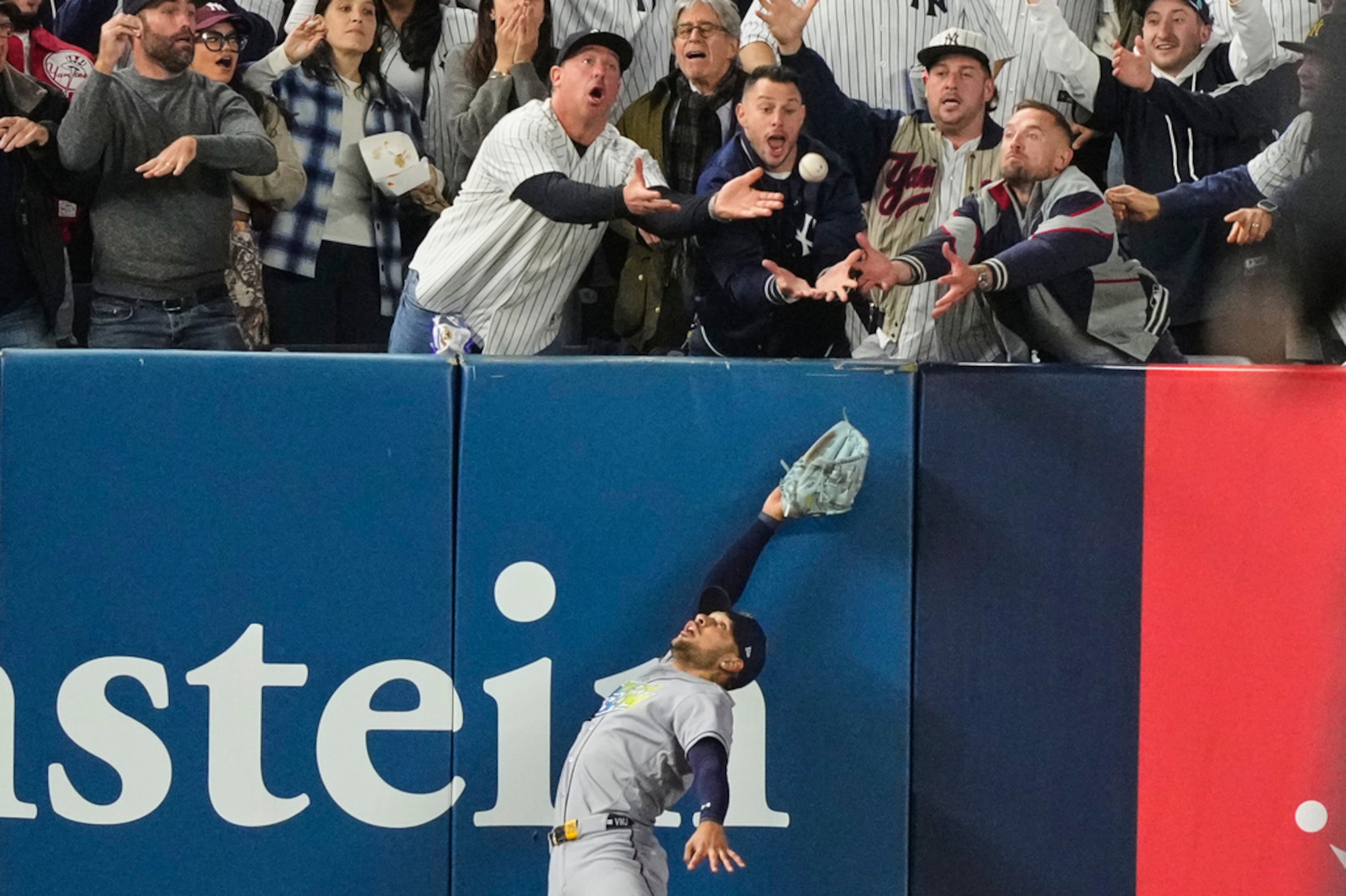 Víctor Mesa Jr., de los Rays de Tampa Bay, trata de atrapar una pelota interferida por fanáticos tras el batazo de Anthony Volpe, de los Yankees, en el sexto inning del tercer juego de la serie divisional de la Liga Americana.