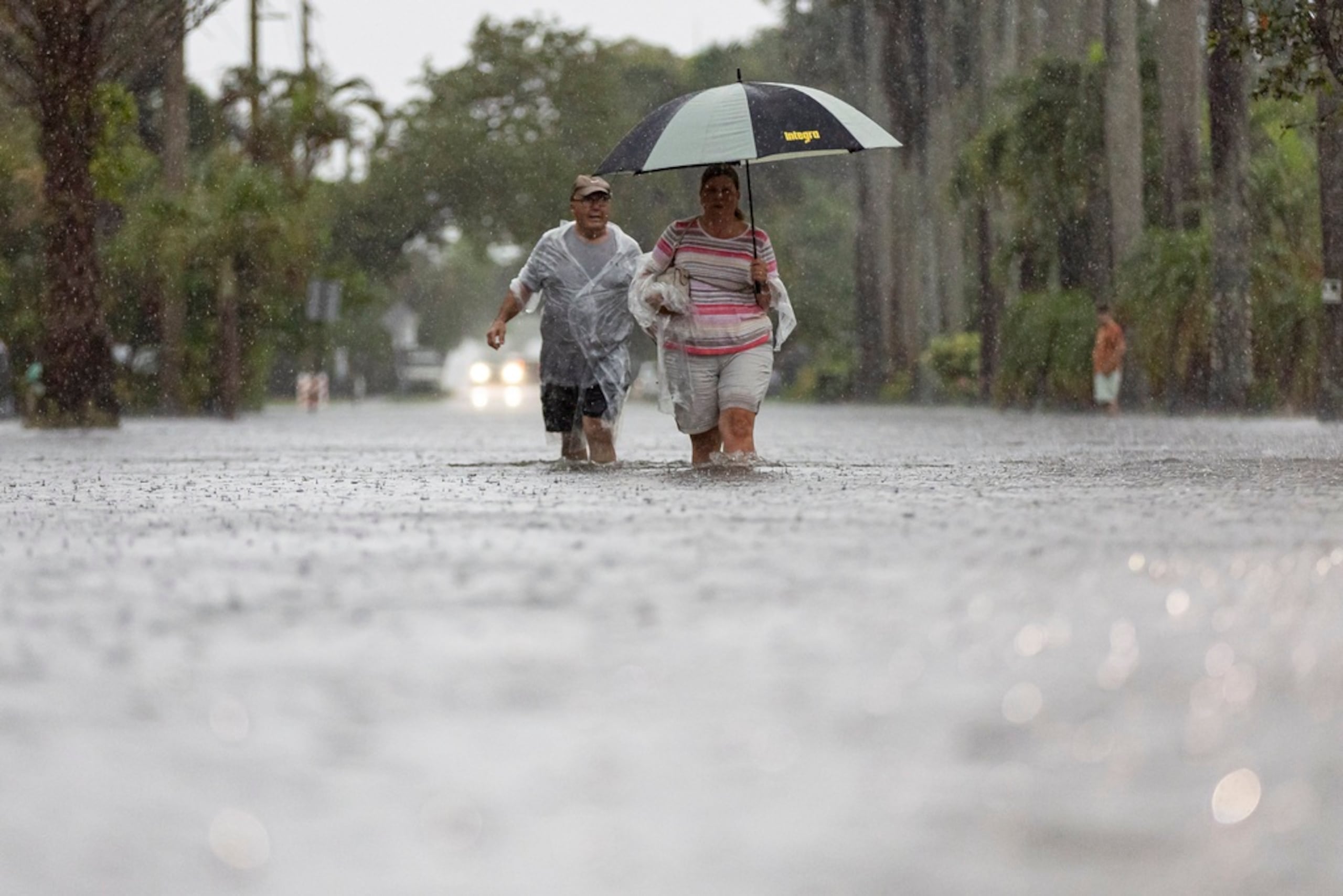 Jim Comunale y Pam Mervos caminan por la calle Arthur mientras fuertes lluvias inundan el vecindario el 12 de junio de 2024 en Hollywood, Florida.