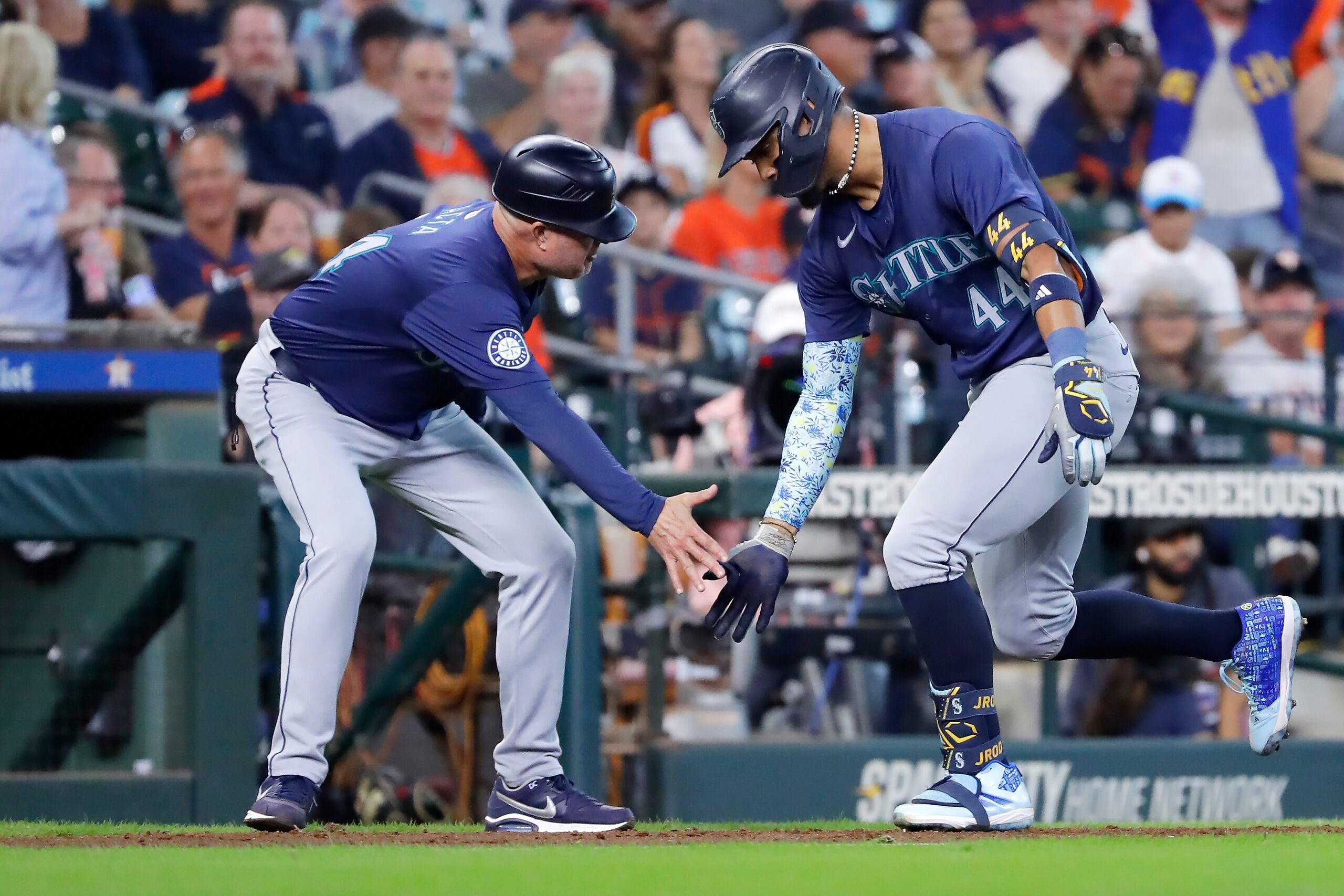 El coach de tercera base de los Marineros de Seattle, Manny Acta, izquierda, y Julio Rodriguez, derecha, celebran jonrón de dos carreras del dominicano en contra de los Astros de Houston, durante la novena entrada del juego de béisbol del miércoles 25 de septiembre de 2024, en Houston. (AP Foto/Michael Wyke)