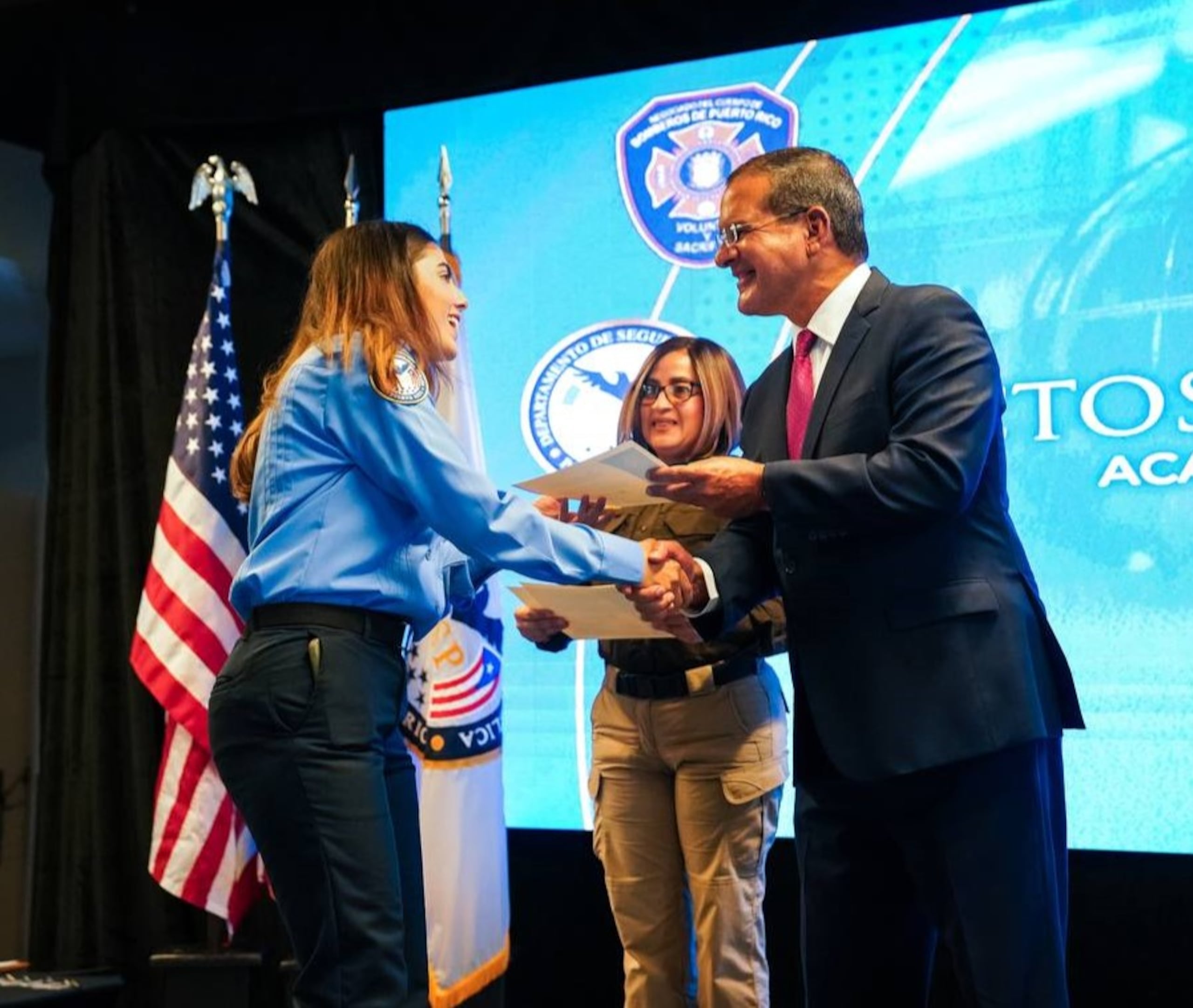 El gobernador Pedro Pierluisi le entrega el diploma a una de las siete mujeres que se graduaron para trabajar como bombero.