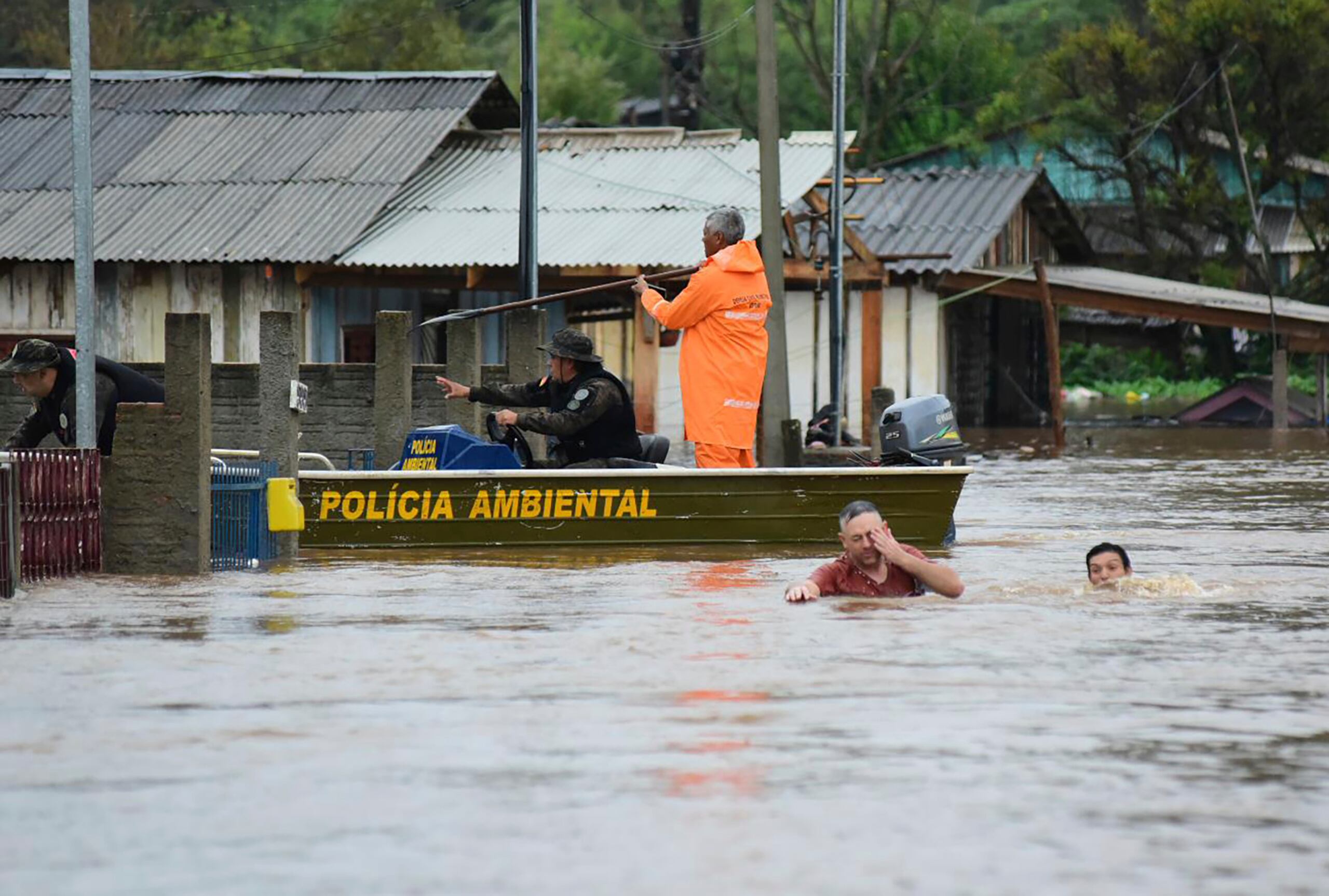 Agentes de policía revisan una casa mientras habitantes vadean una calle inundada por tormentas derivadas de un ciclón que ha provocado mas de 21 muertes y mas de 1,600 afectados.