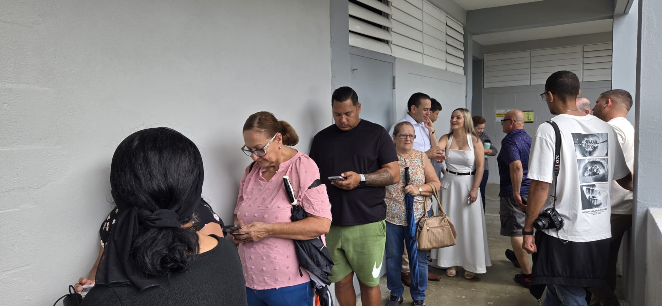 William Villafañe, con camisa blanca, hace la fila para votar en la Escuela Especializada de Bellas Artes Pablo Casals, En Bayamón. Lo acompaña su esposa.
