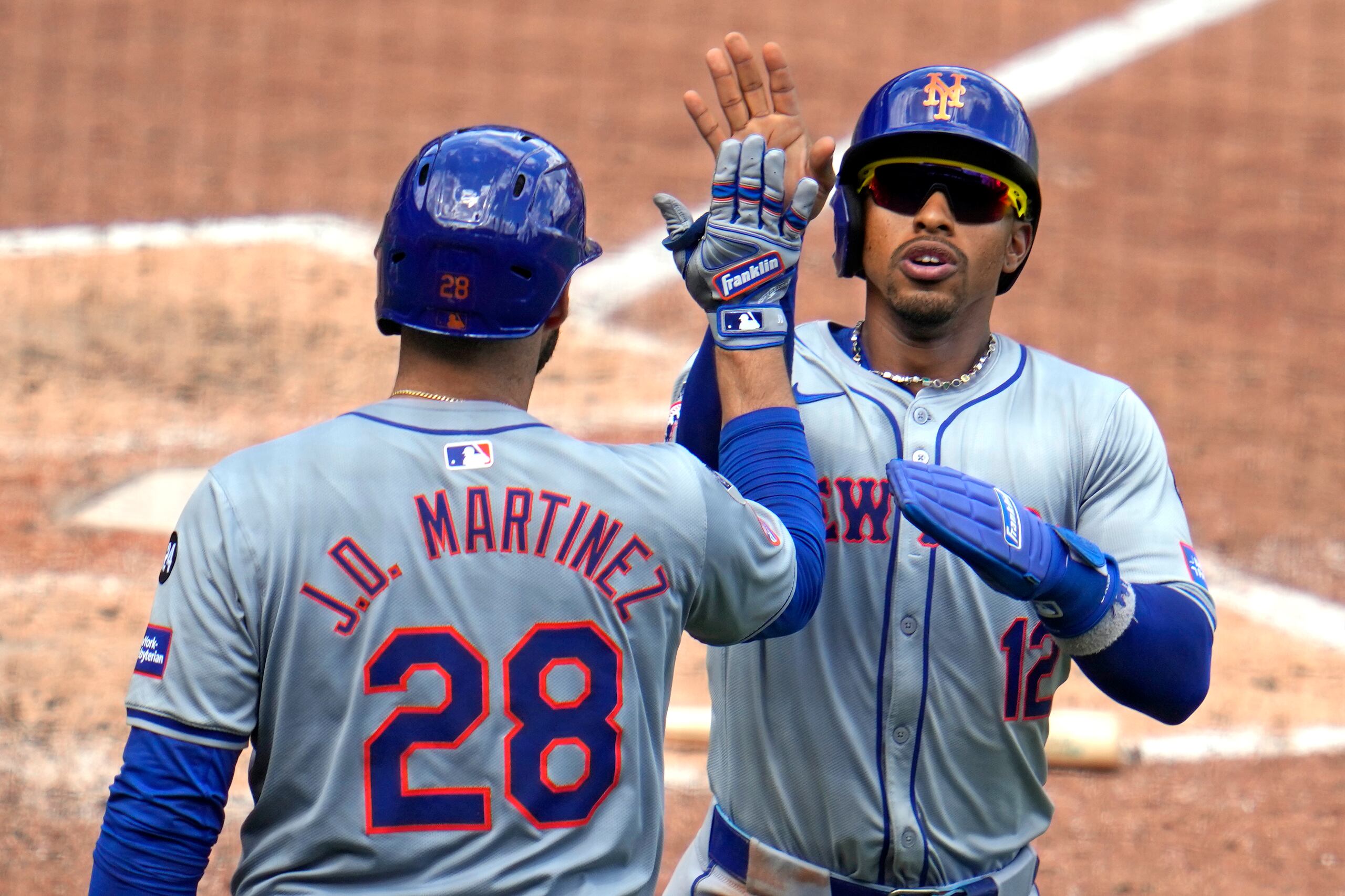 New York Mets' Francisco Lindor (12) is greeted by J.D. Martinez (28) as he returns to the dugout after scoring on a double by Brandon Nimmo off Pittsburgh Pirates relief pitcher Colin Holderman during the eighth inning of a baseball game in Pittsburgh, Sunday, July 7, 2024. (AP Photo/Gene J. Puskar)