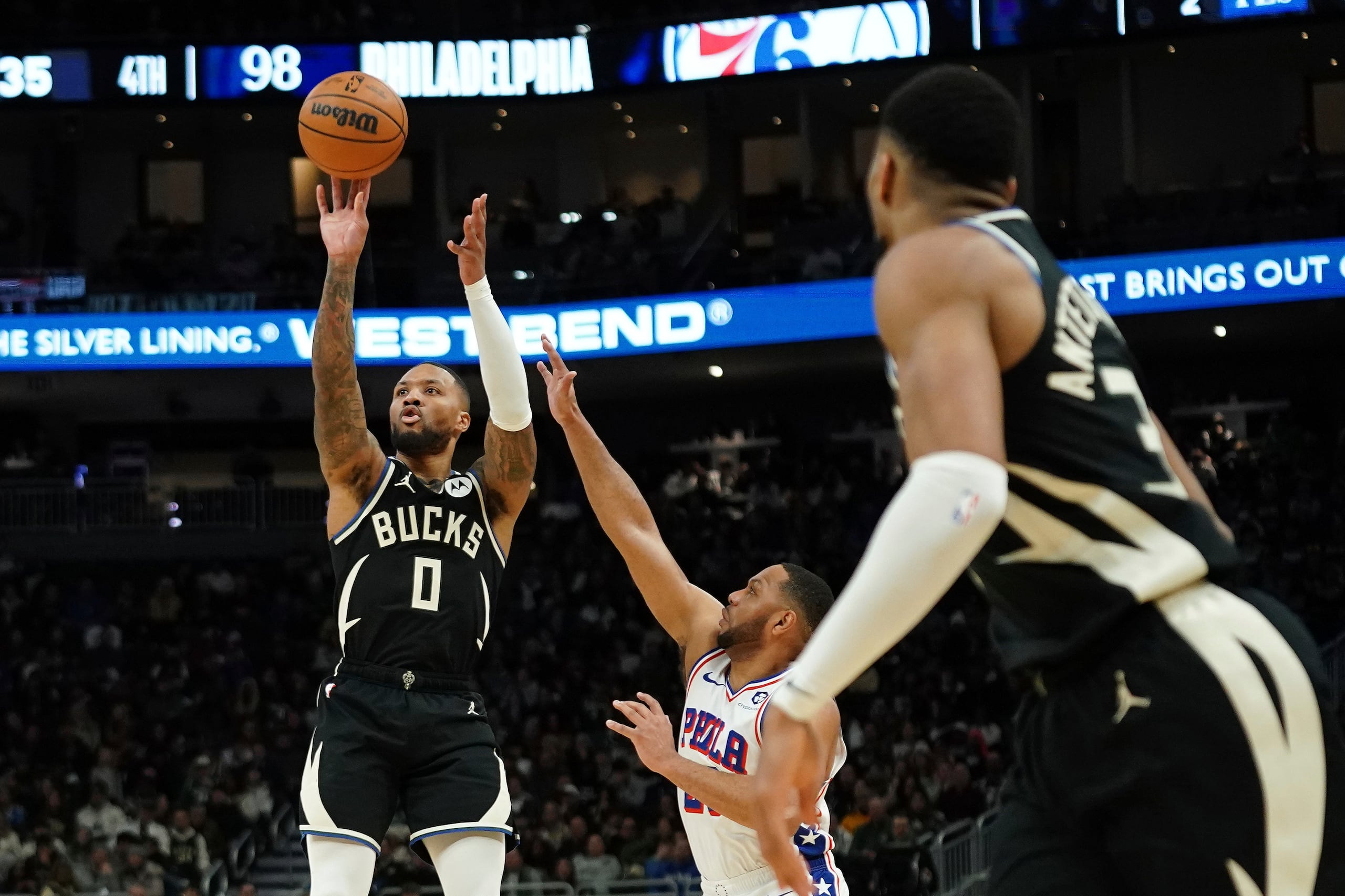 Damian Lillard (0), de los Bucks de Milwaukee, dispara a la canasta mientras Eric Gordon, centro, de los 76ers de Filadelfia, hace un intento por defender, durante la segunda mitad del juego de baloncesto de la NBA, el domingo 9 de enero de 2025, en Milwaukee. (AP Foto/Aaron Gash)
