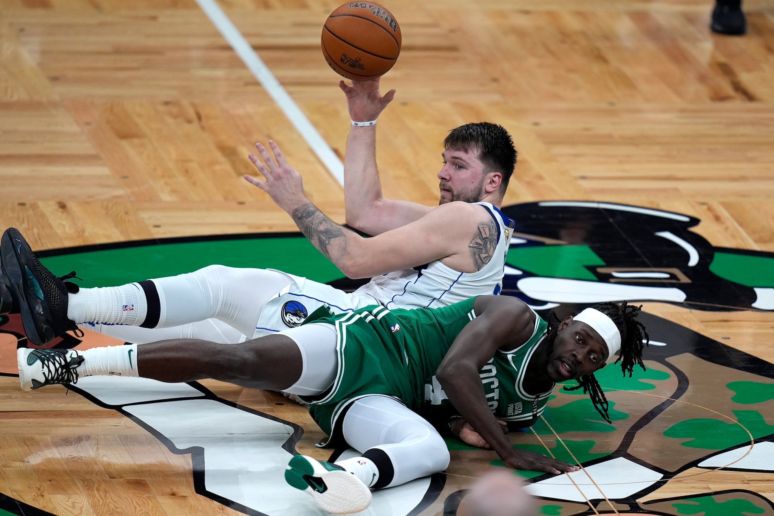Luka Doncic busca pasar el balón mientras está tendido en el tabloncillo de los Celtics de Boston.