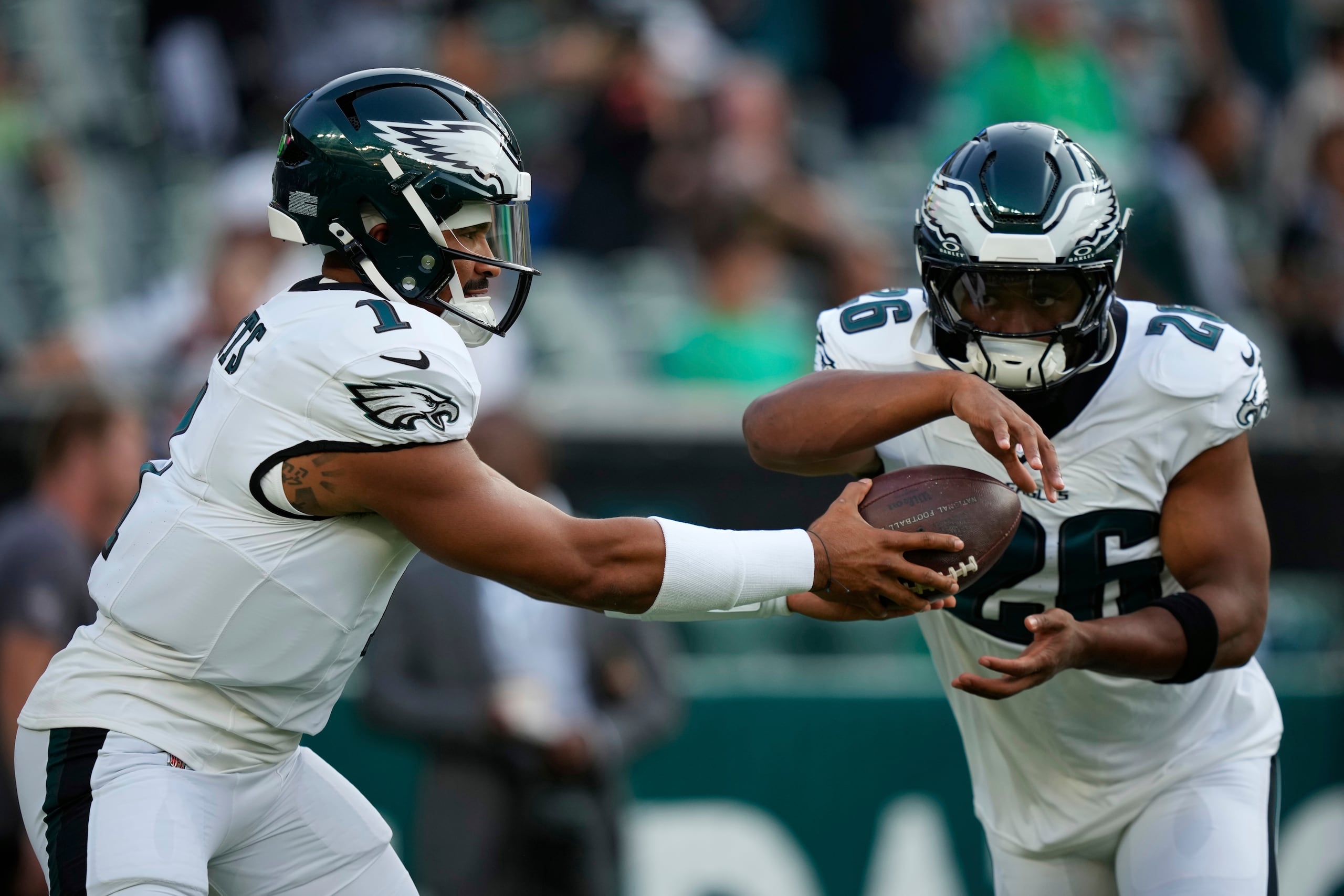 Jalen Hurts (1), quarterback de los Eagles de Filadelfia, entrega el balón a Saquon Barkley (26), corredor, durante los ejercicios de calentamiento previo a un partido de pretemporada de la NFL.
