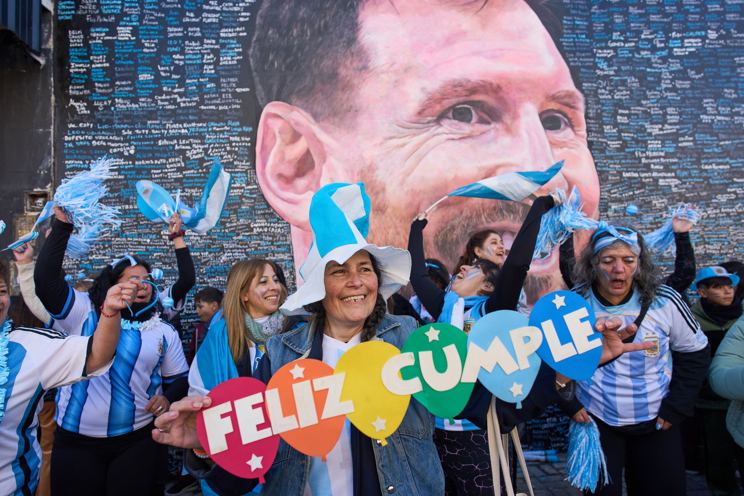 Una mujer sostiene un cartel con el mensaje de "Feliz Cumple" frente a un mural del astro argentino Lionel Messi, en Buenos Aires.