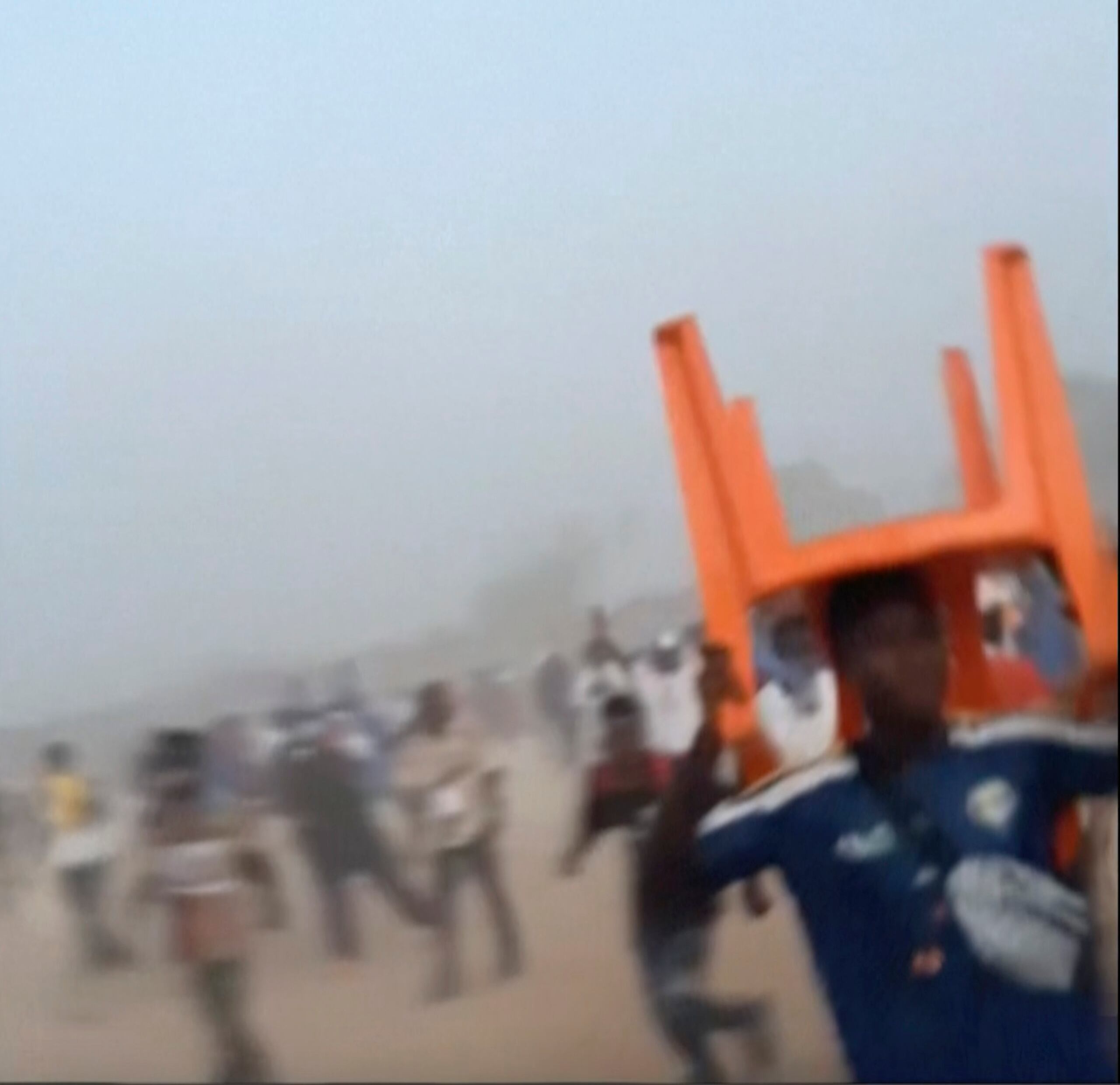 En esta imagen tomada de un video proporcionado por Nimba Sports Zaly, un hombre sostiene una silla sobre su cabeza durante una estampida en un partido de fútbol en el estadio de Nzérékoré, en Nzérékoré, Guinea, el domingo 1 de diciembre de 2024. (Nimba Sports Zaly via AP)