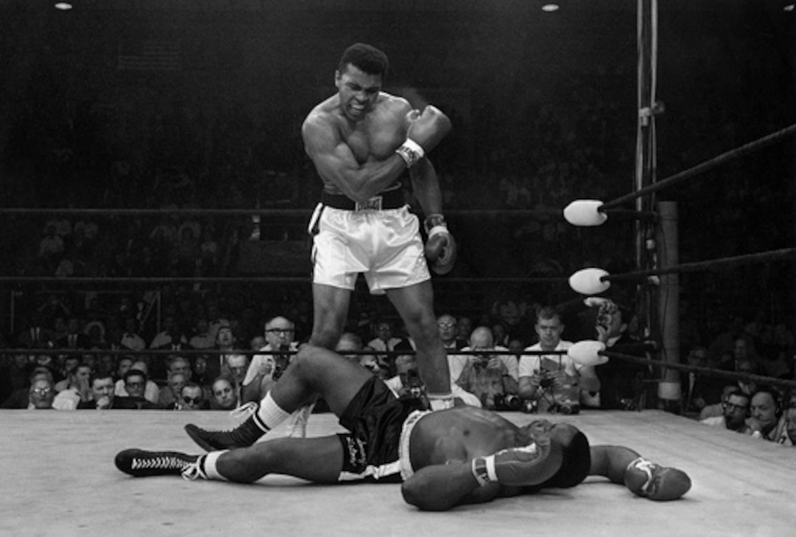 ARCHIVO - Muhammad Ali, campeón de los pesos pesados, de pie junto a Sonny Liston, su rival caído, grita y gesticula poco después de derribar a Liston con un fuerte derechazo a la mandíbula el 25 de mayo de 1965, en Lewiston, Maine. (AP Photo/John Rooney, archivo)