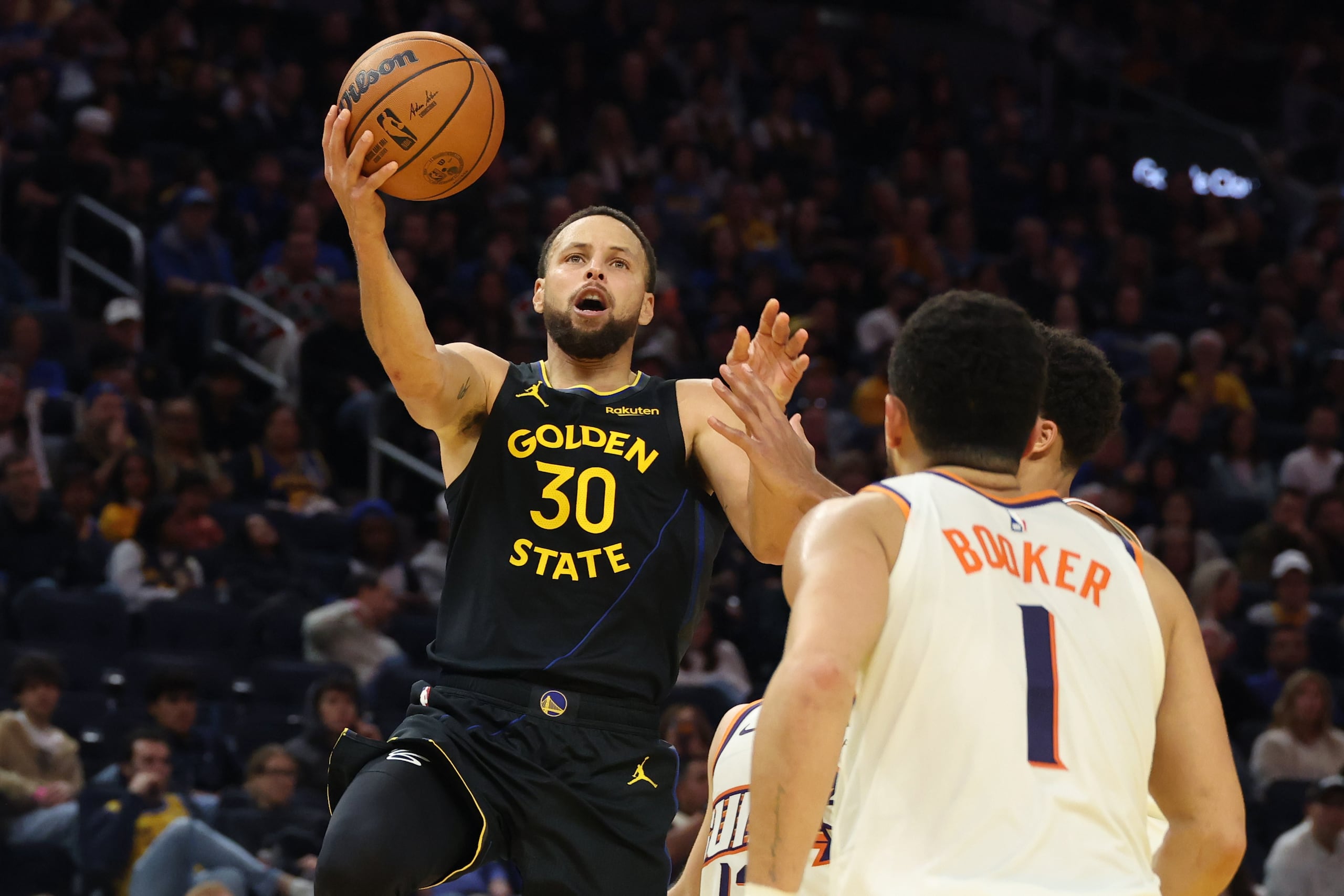 Stephen Curry, base de los Warriors de Golden State, dispara frente a Devin Booker de los Suns de Phoenix, el sábado 20 de diciembre de 2025 (AP Foto/Jed Jacobsohn)
