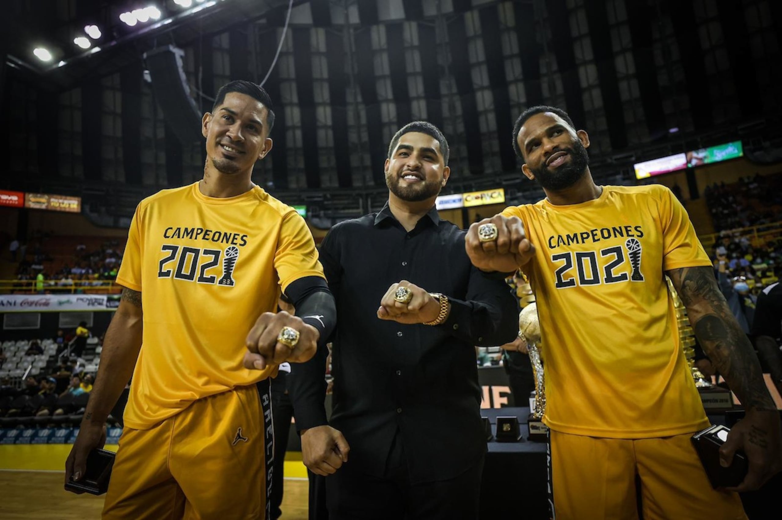 El exapoderado de los Capitanes de Arecibo Frabián Eli (centro) posa con los canasteros David Huertas (izquierda) y Walter Hodge Jr. luego de la entrega de anillos del campeonato de 2021.