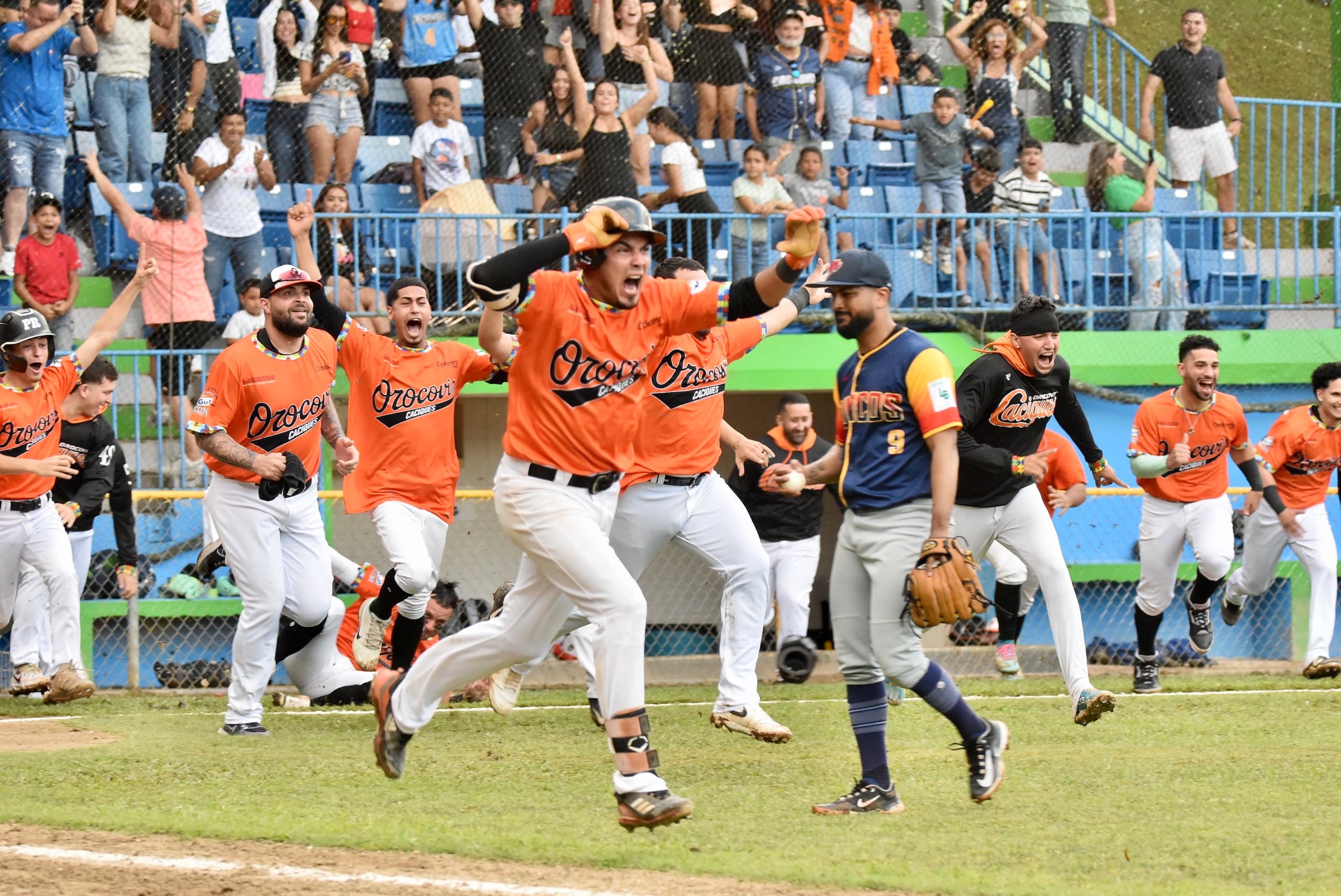 Kelvin Pérez corre hacia primera base luego de conectar el hit que decidió el partido y la coronación de los Caciques. Detrás de él se ven a sus compañeros irrumpir al terreno para la celebración.