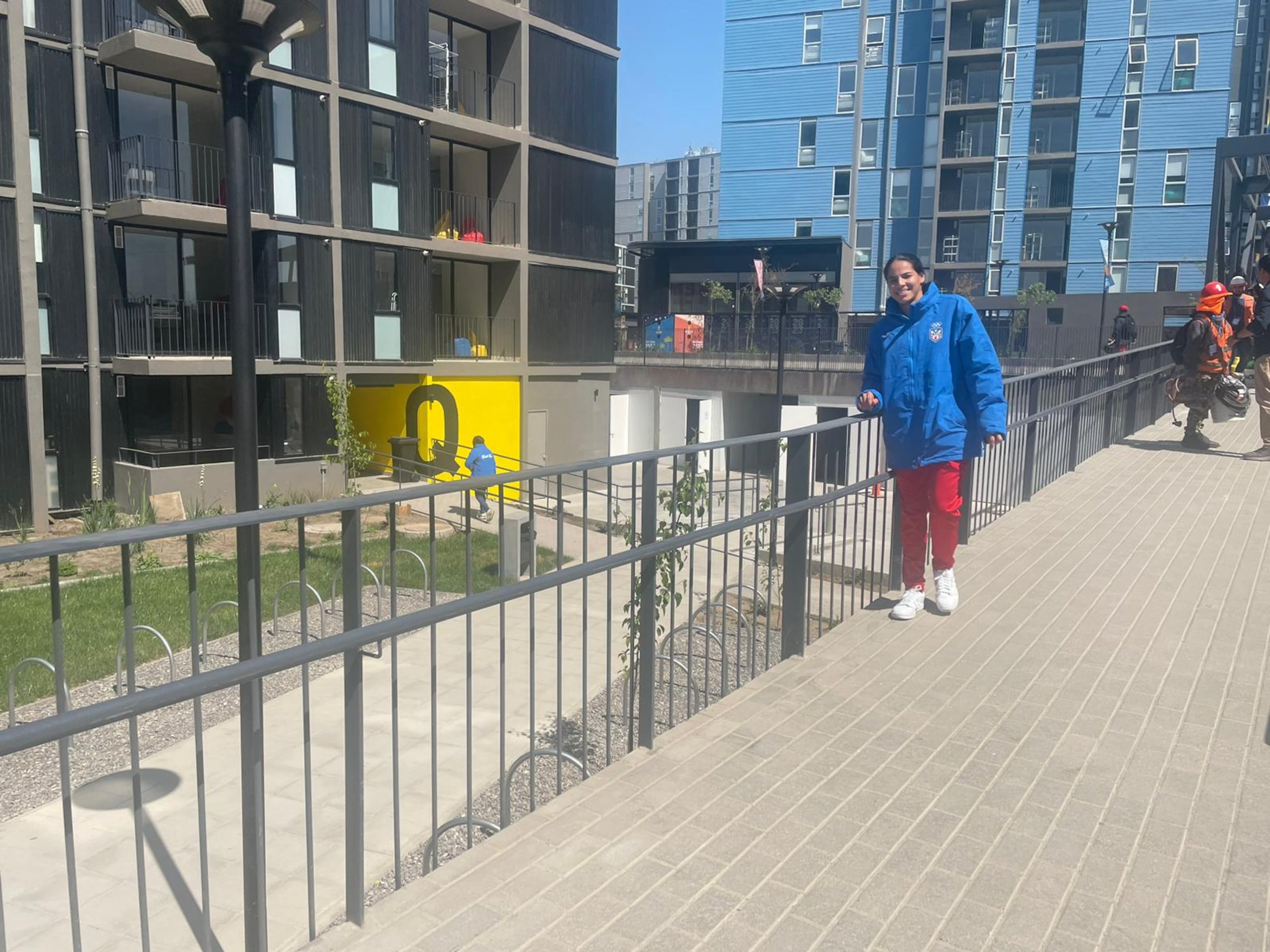 Anelisse Vargas, del equipo femenino de baloncesto 3x3, posa con la Villa Panamericana al fondo y la ropa caliente que le proveyó el Copur para las bajas temperaturas en Santiago.