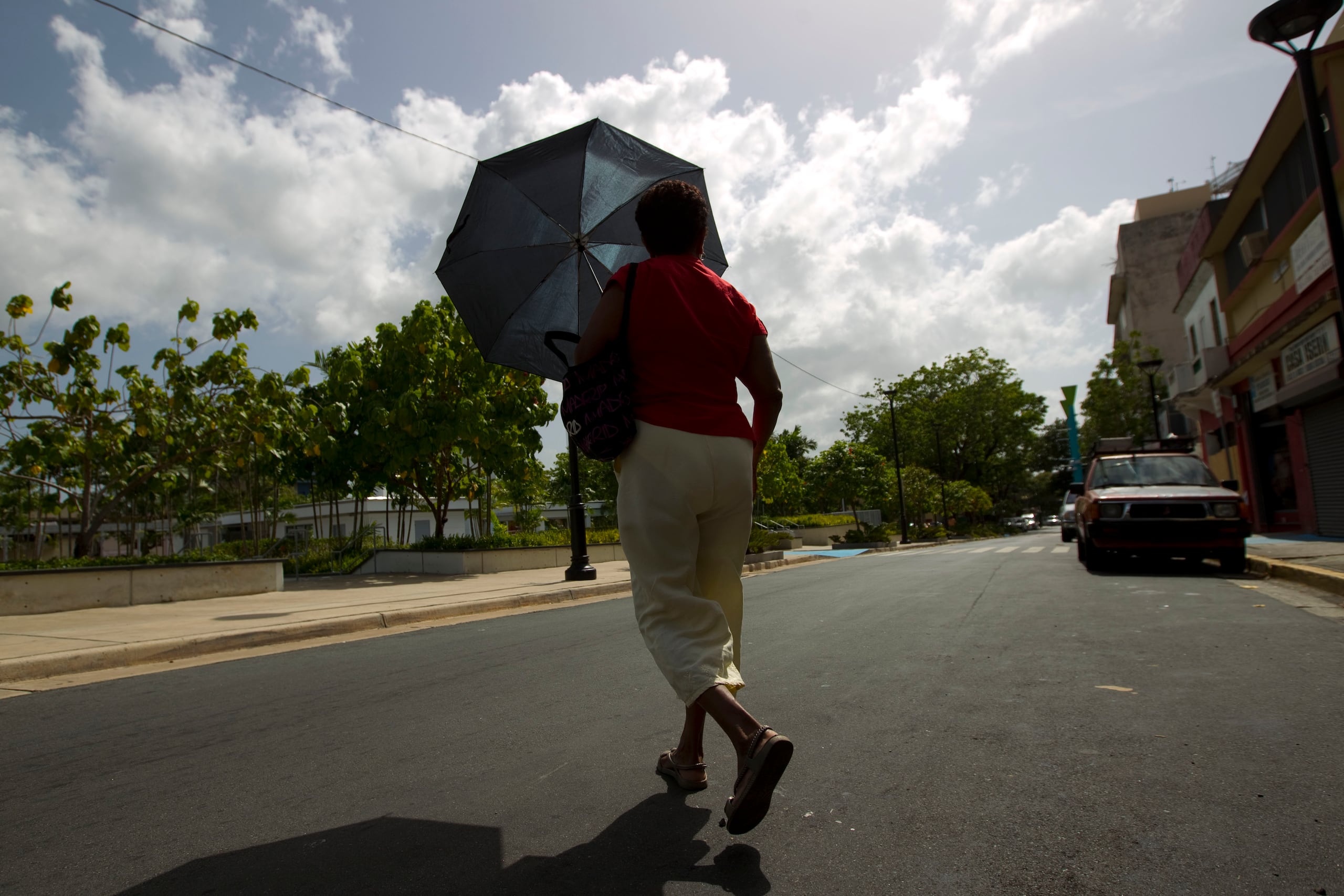 San Juan - Junio 14 , 2012 - PR HOY - Foto para ilustrar una hitoria sobre el fuerte calor . EN LA FOTO una mujer camina con un paraguas ( sombrilla ) para cubrirse de sol.