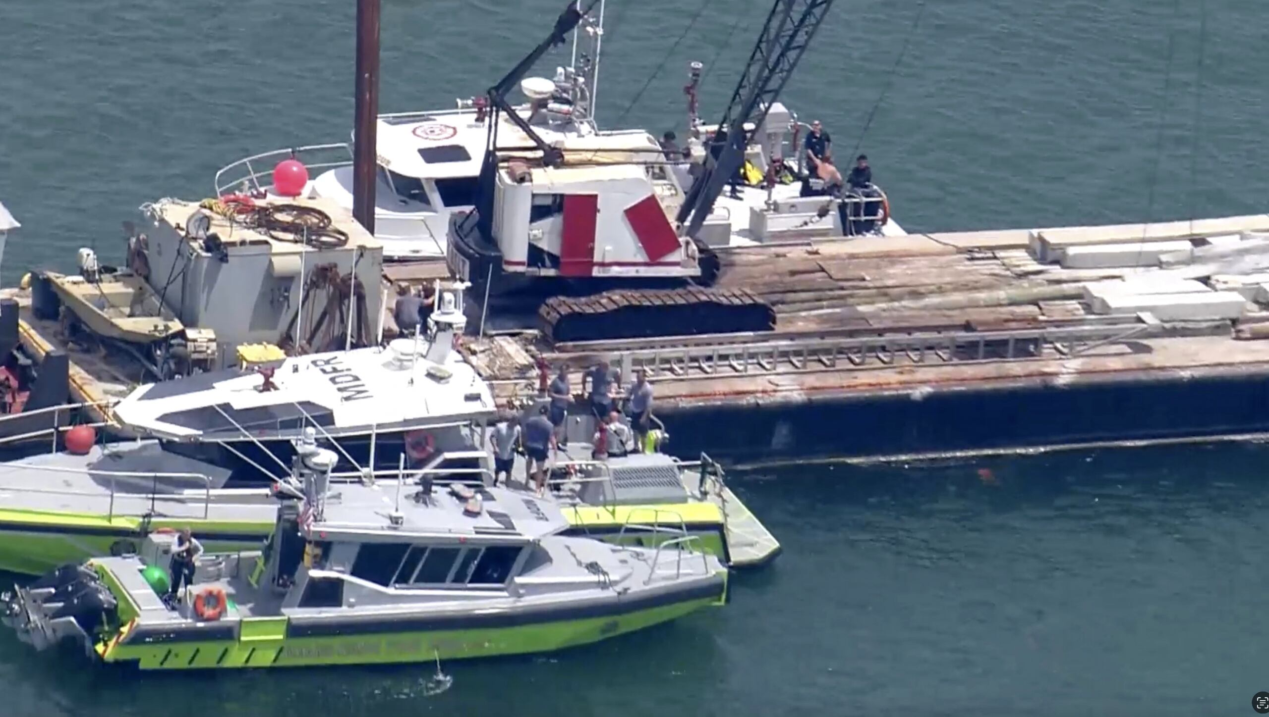 This image taken from video provided by WSVN-TV shows Miami-Dade Fire Rescue and others in boats around what appears to be a barge involved in an accident with a group of kids and an adult on a sailing boat during a sailing camp, Monday, July 28, 2025, in Miami. (WSVN-TV via AP)