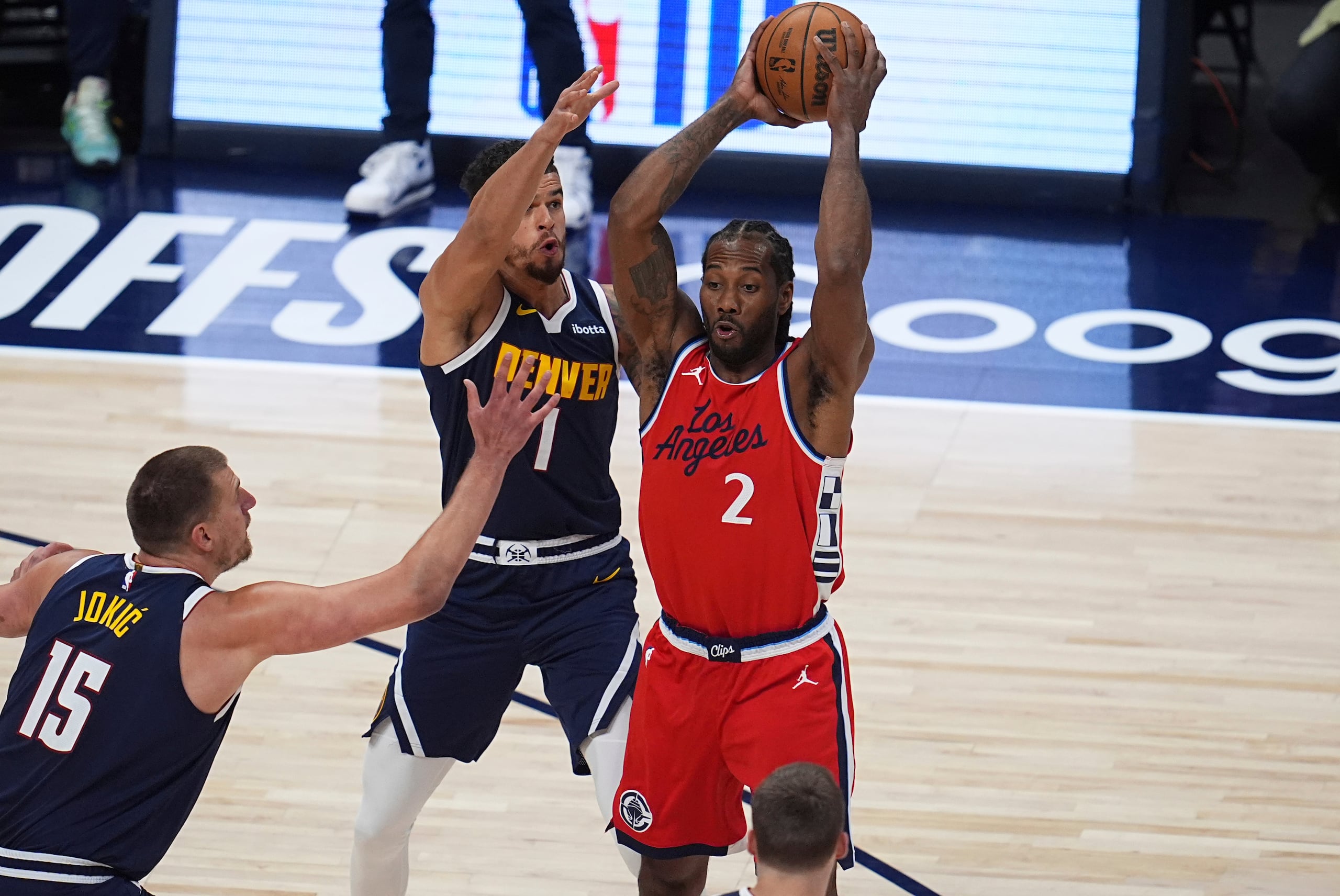 Kawhi Leonard, derecha, de los Clippers de Los Ángeles, busca pasar el balón mientras Nikola Jokic, izquierda, y Michael Porter Jr., centro, de los Nuggets de Denver, defienden en la primera mitad del segundo juego de la serie de playoffs de primera ronda del baloncesto de la NBA, el lunes 21 de abril de 2025, en Denver. (AP Foto/David Zalubowski)