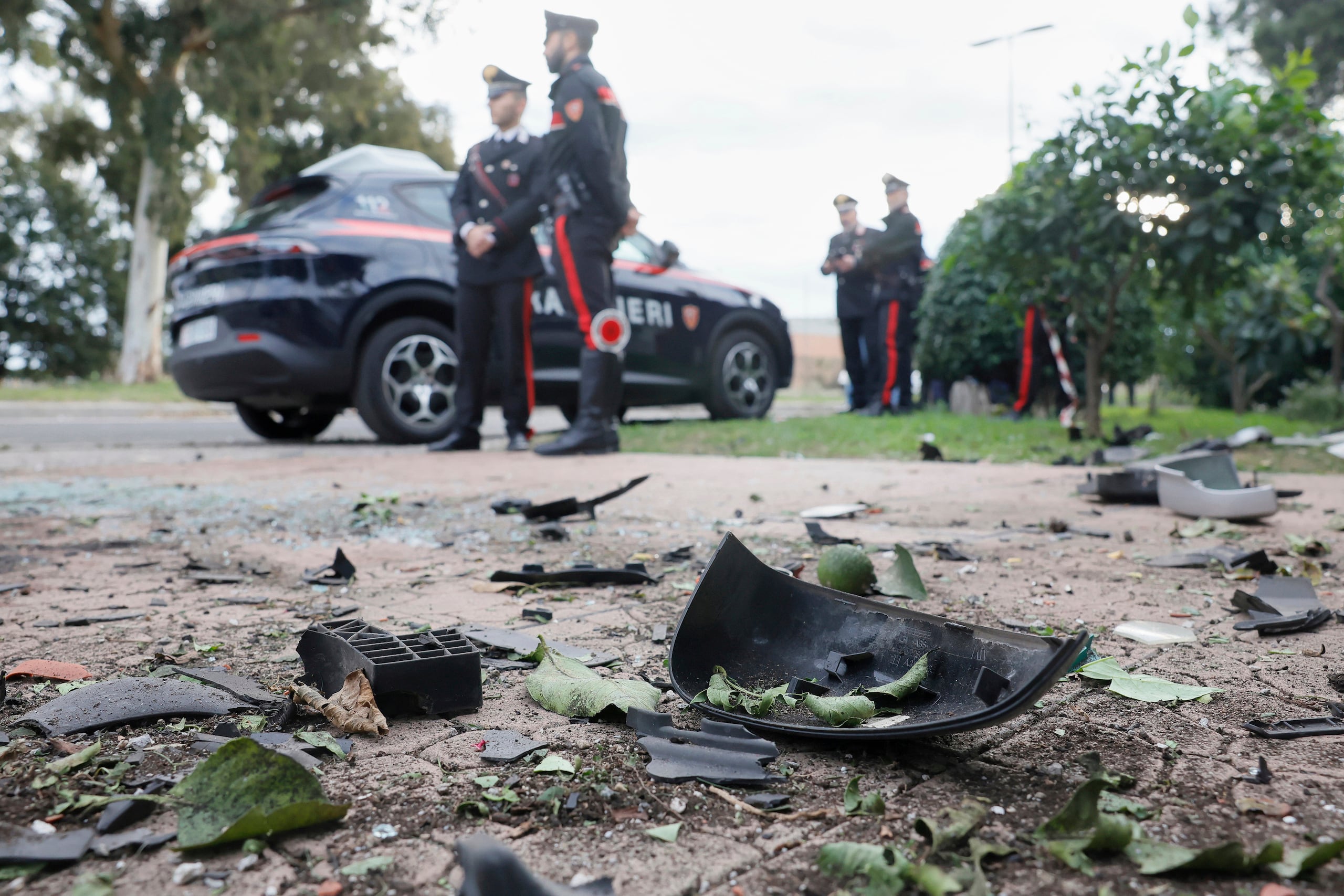 Partes de un auto en el piso mientras efectivos de los Carabinieri hacen guardia en el exterior de la casa del periodista de investigación Sigfrido Ranucci tras la explosión de un artefacto debajo de su auto, en Pomezia, Italia, el 17 de octubre de 2025. (Cecilia Fabiano/LaPresse vía AP)