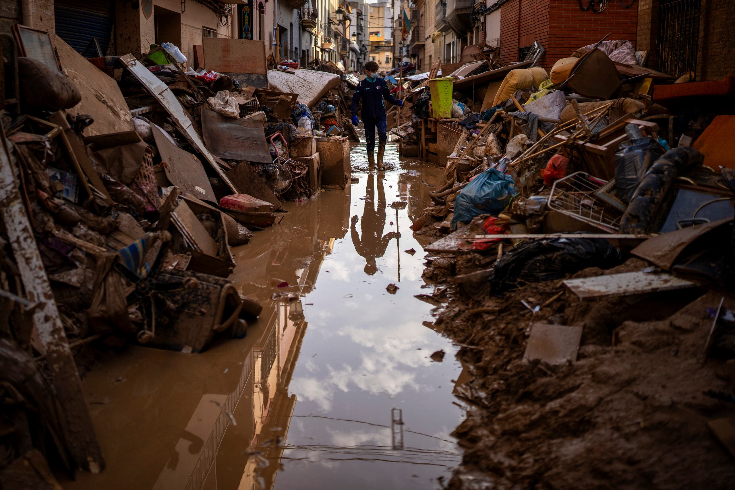 Una persona camina por la calle entre muebles y basura amontonada a los lados afectada por inundaciones en Paiporta, Valencia, España.