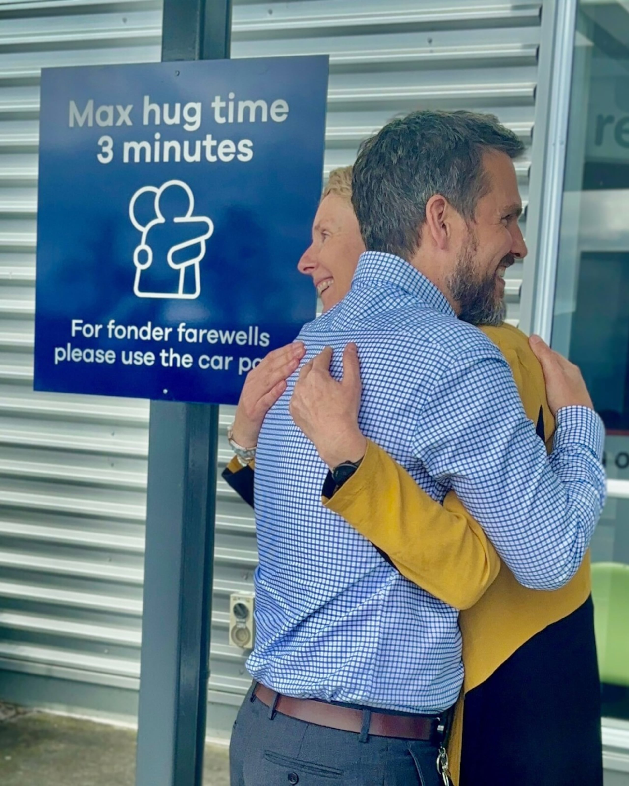 El director ejecutivo del aeropuerto neozelandés de Dunedin, Daniel De Bono, y la directora de desarrollo comercial, Megan Crawford, abrazados junto el cartel que indica "máximo 3 minutos de abrazos" colocado en el aeropuerto de Dunedin, Nueva Zelanda, una radical medida que se ha vuelto viral.