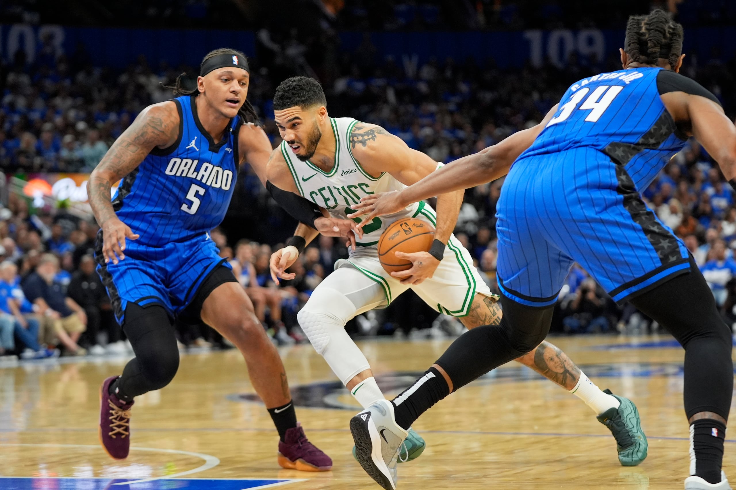 El alero de los Celtics de Boston, Jayson Tatum, centro, conduce entre el alero del Magic de Orlando Paolo Banchero (5) y el pívot Wendell Carter Jr. (34) durante la primera mitad del Juego 4 de una serie de playoffs de baloncesto de la NBA de primera ronda, el domingo 27 de abril de 2025, en Orlando, Florida (AP Foto/John Raoux)
